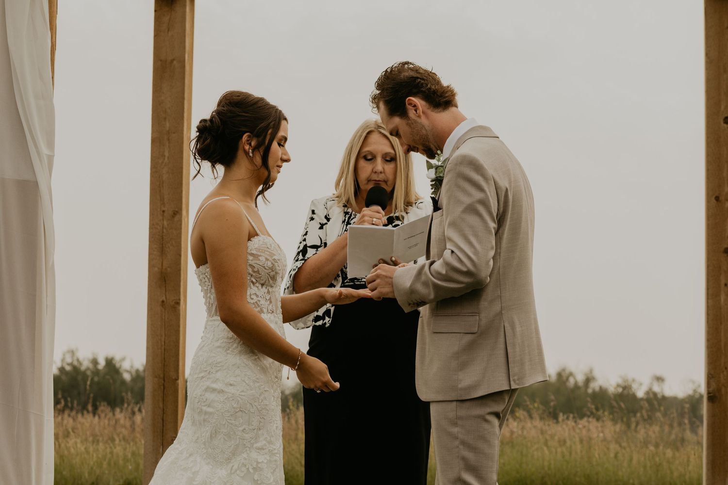 Outdoor wedding ceremony with couple and officiant under wooden arch.