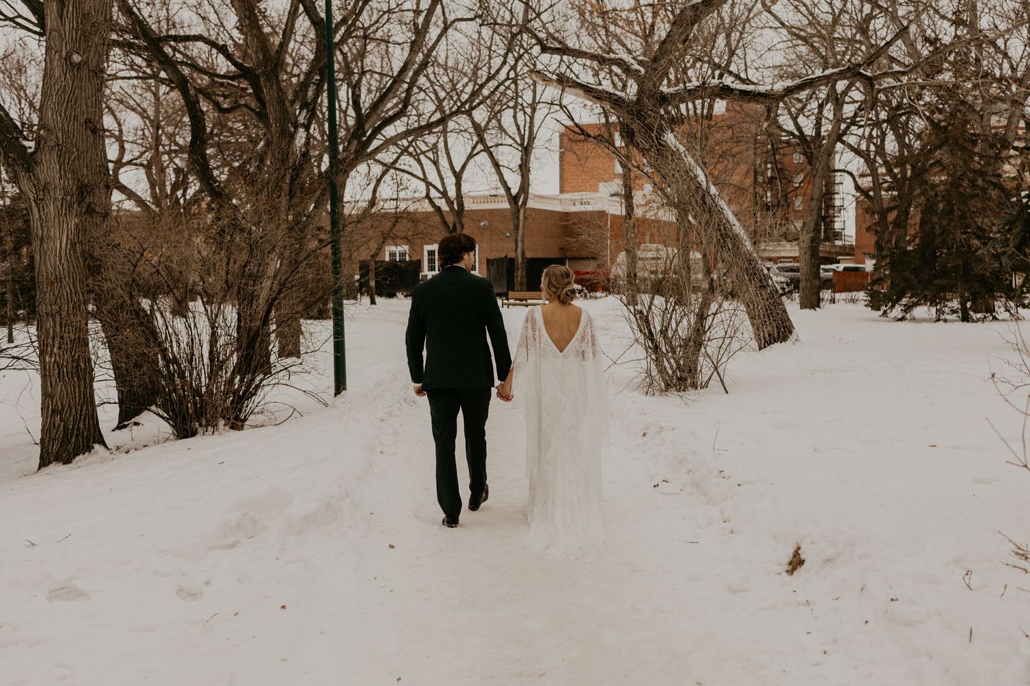 Newlywed couple walks through snowy winter landscape after wedding ceremony.