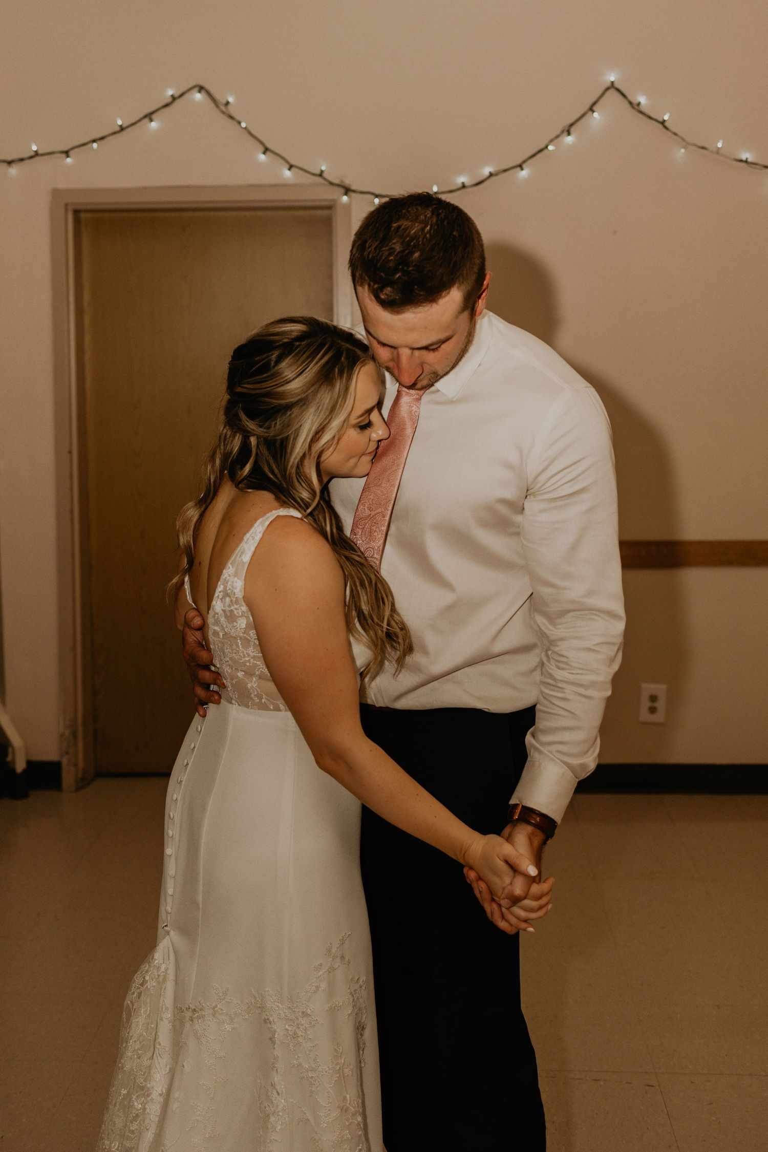 Intimate slow dance moment at a wedding reception under string lights.