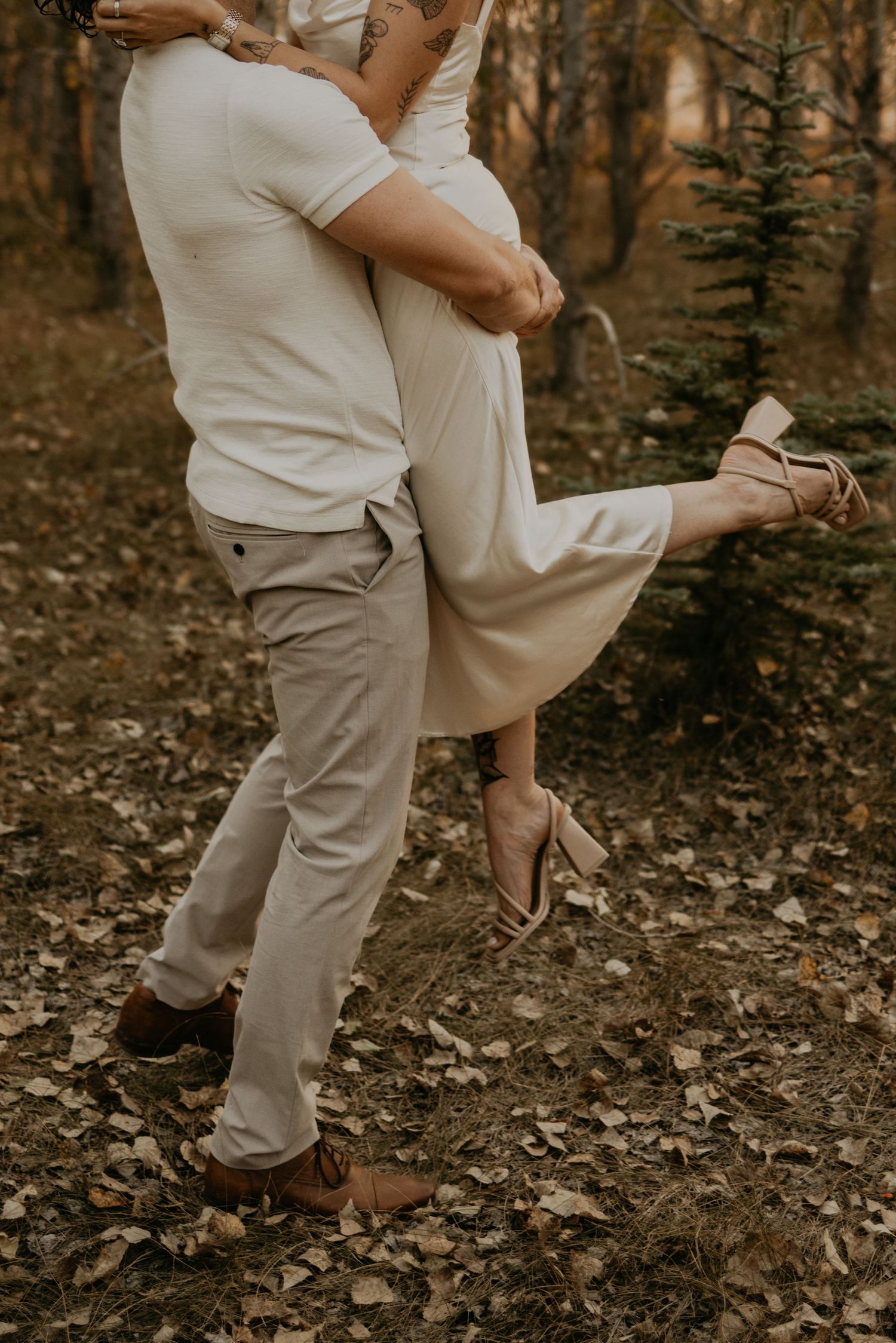 An intimate dance moment captured between two people in light colored outfits among autumn trees.