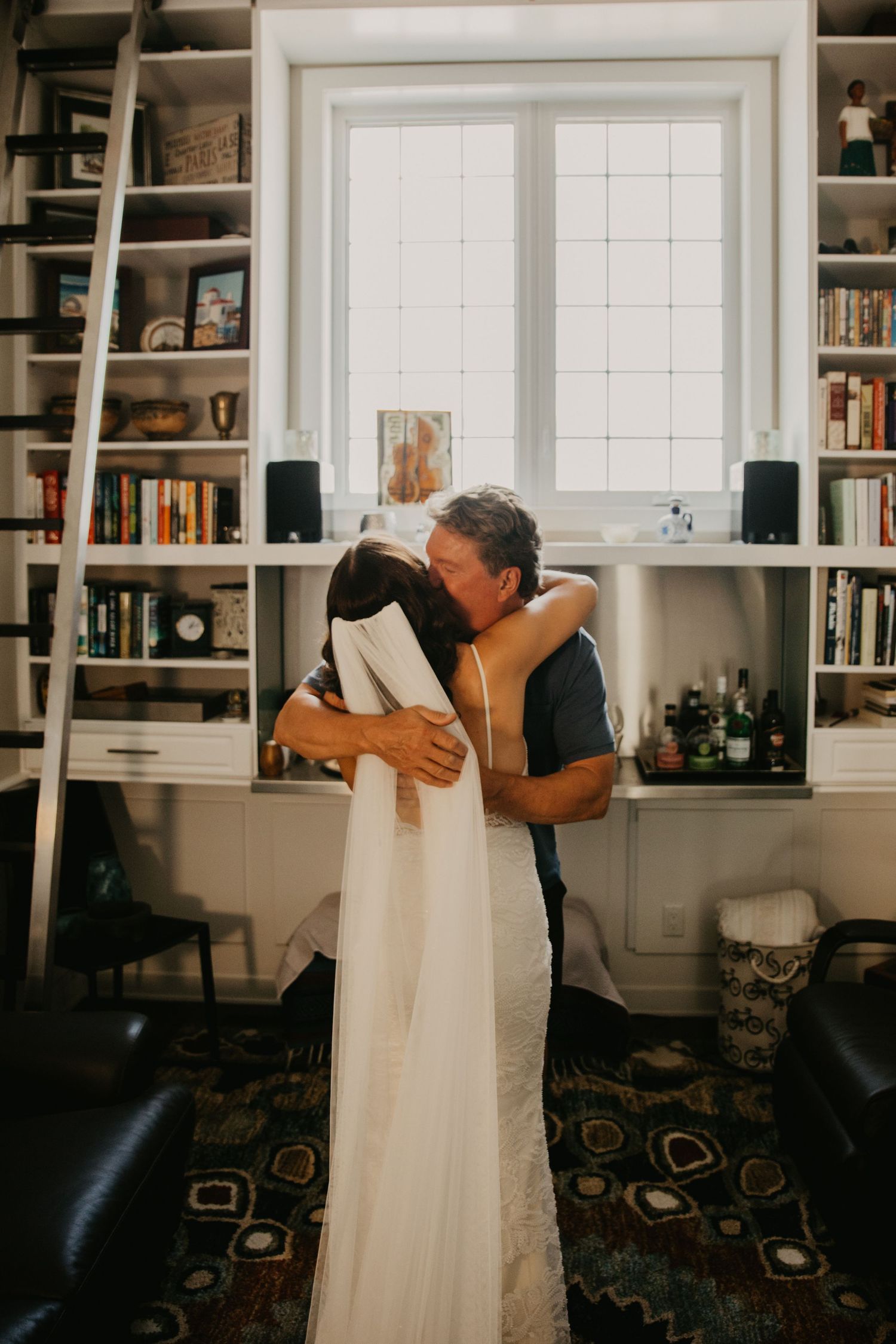 Intimate moment with wedding dress displayed in library room with built-in bookshelves.