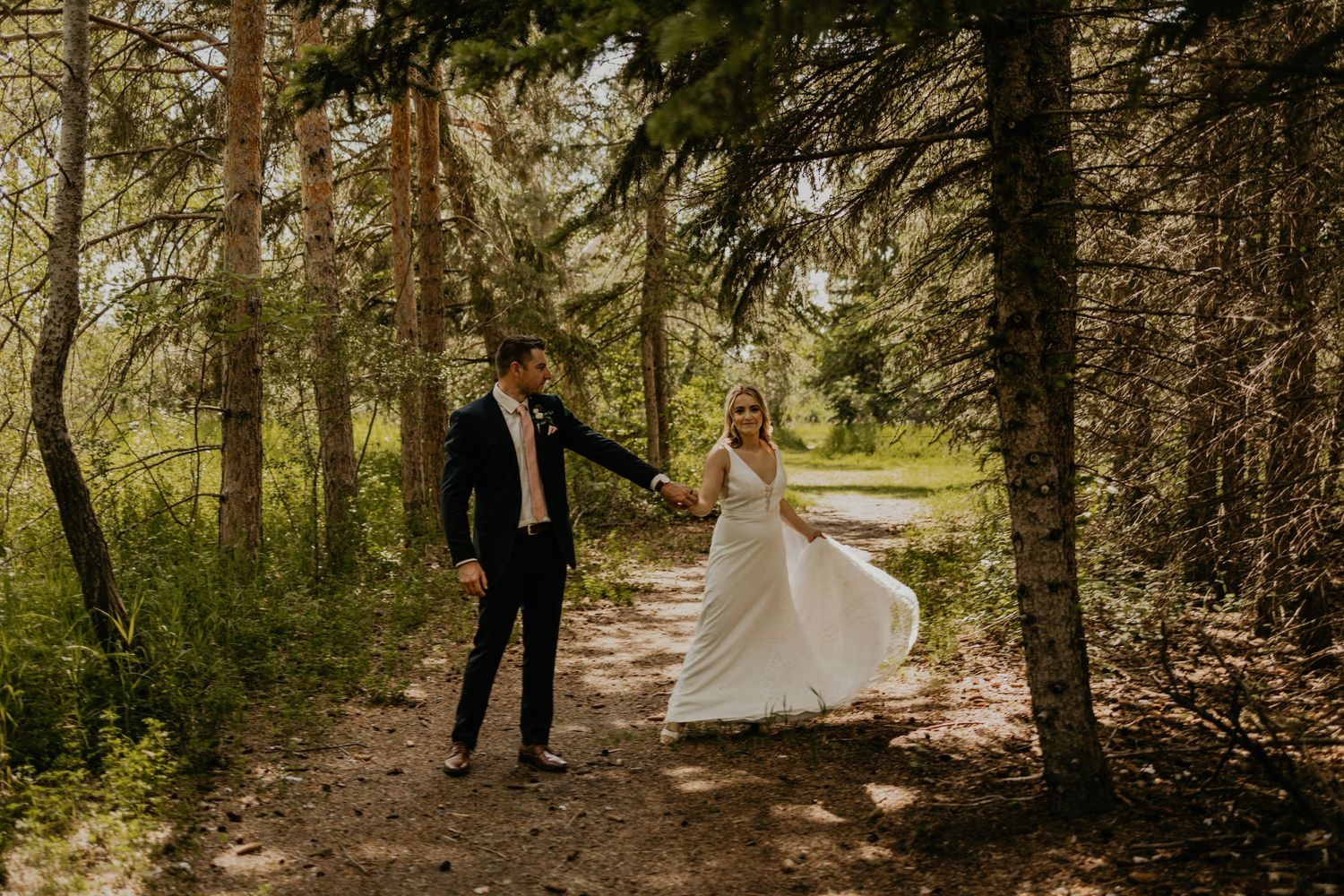 Couple dancing and twirling on a forest path in wedding attire.