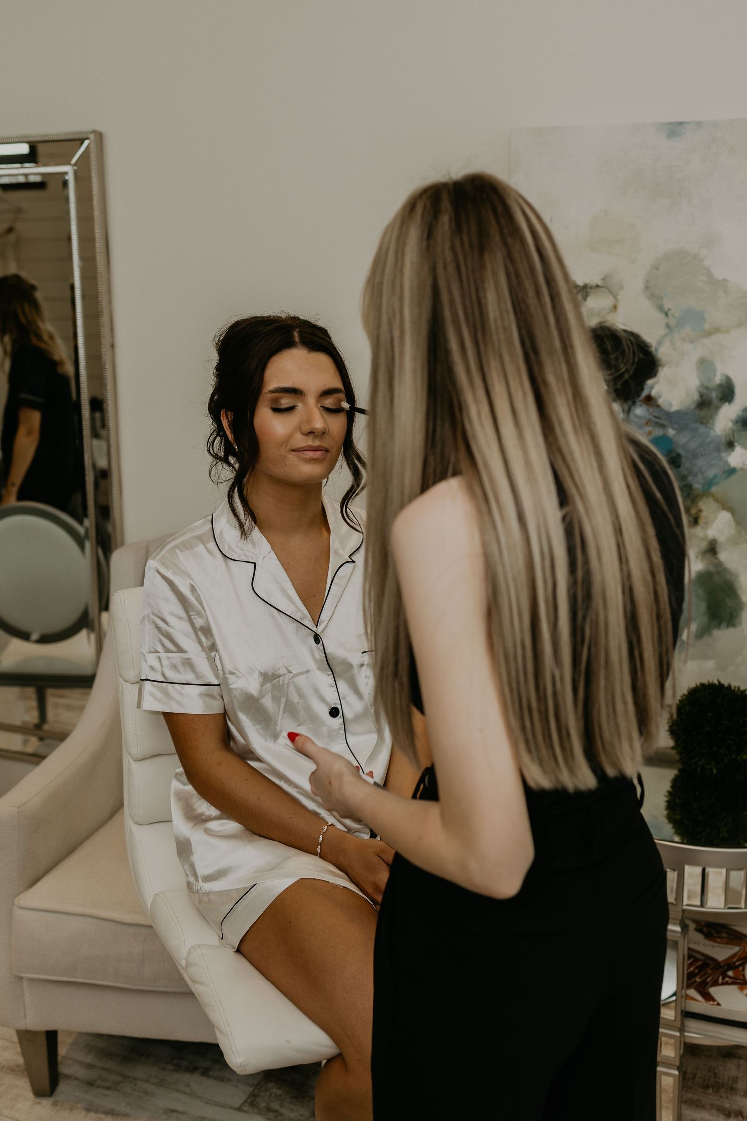 A makeup session in progress with soft natural lighting and abstract art in the background.
