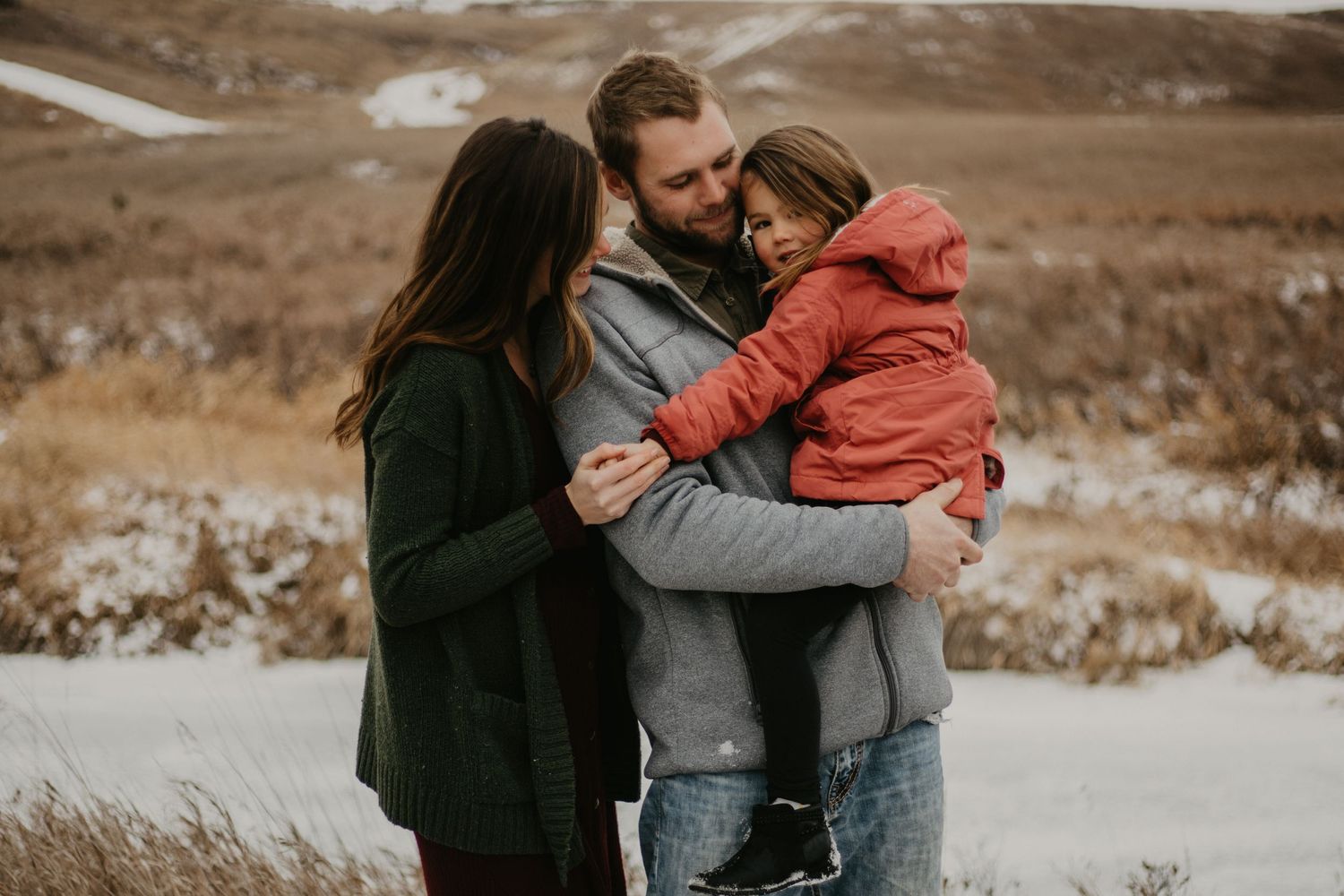An intimate family portrait on a snowy hillside with warm winter clothing and embraces.