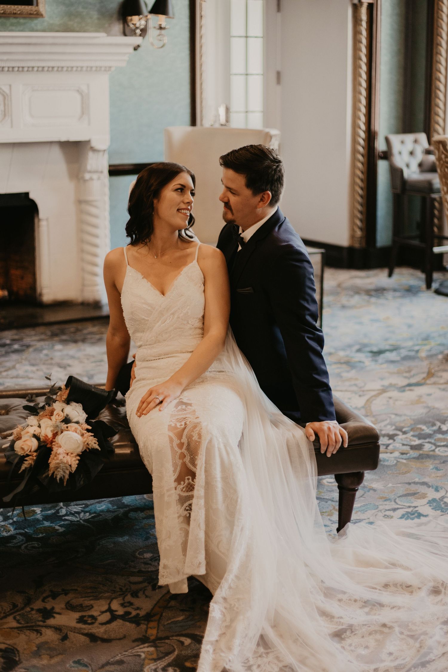 Candid wedding moment captured by a white fireplace with the couple sharing a laugh.