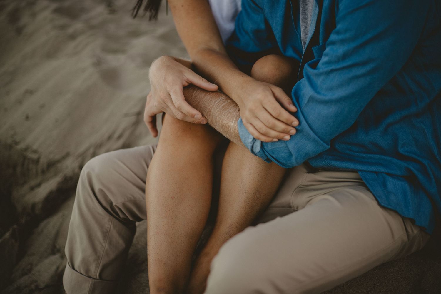 Close-up shot of couple's hands resting on knees while sitting together.