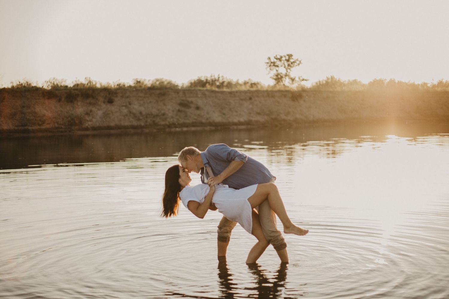 A playful dip pose in shallow water during a sunset beach photoshoot.