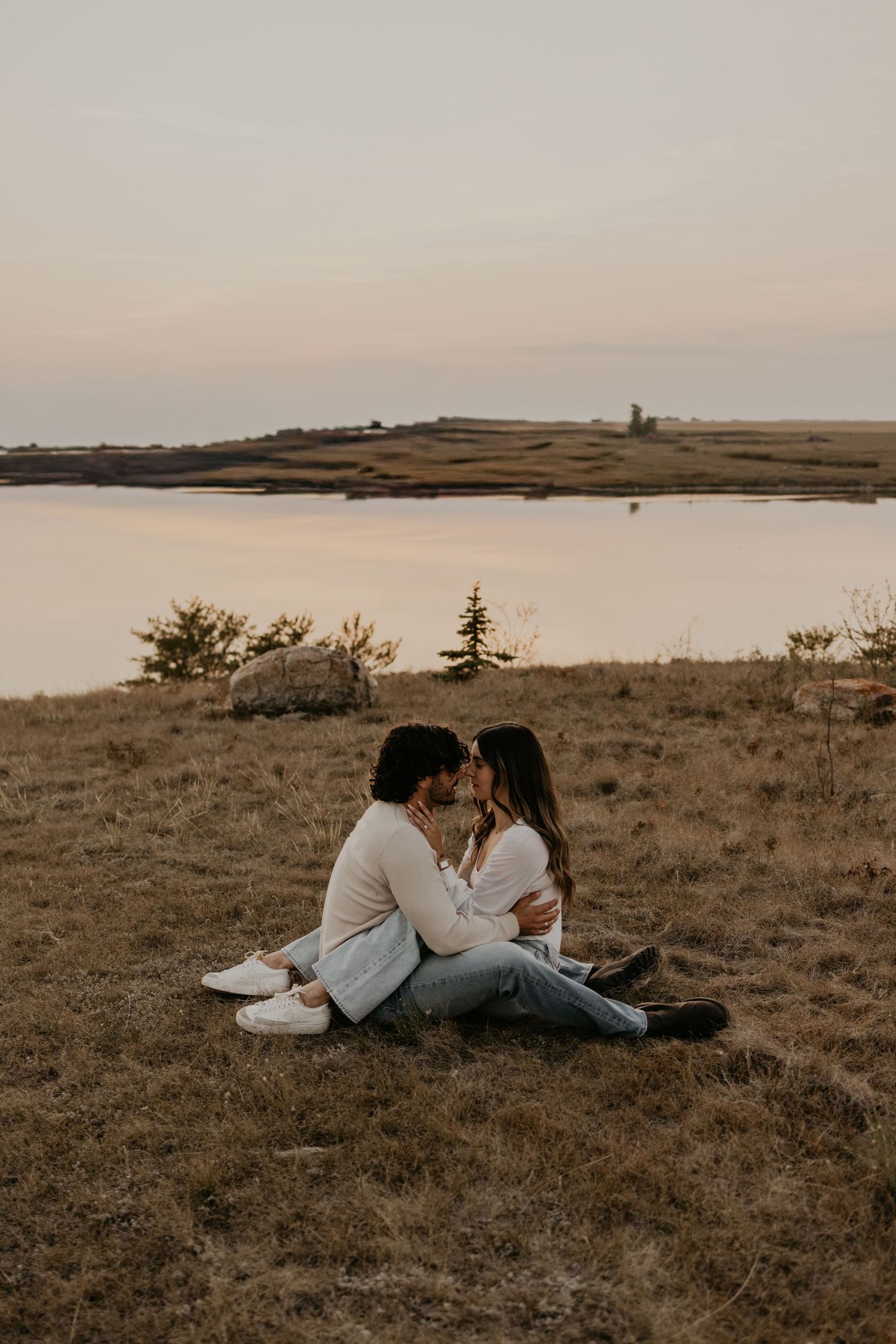 A couple relaxing together on grassy terrain with a scenic landscape view during sunset.