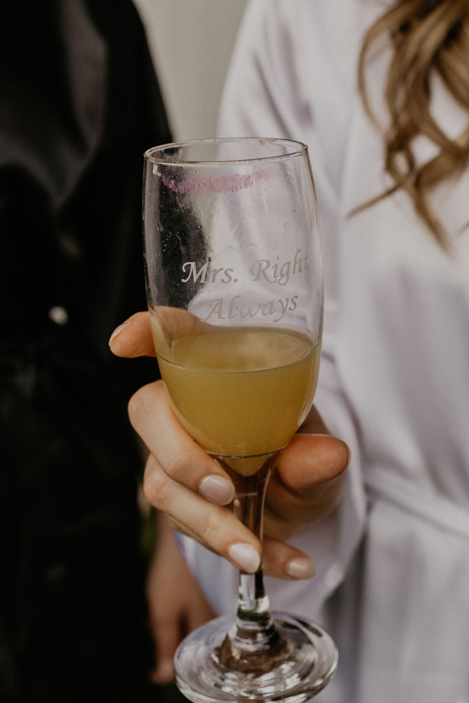 A champagne glass with 'Mrs. Right' engraving held by someone in a white robe.