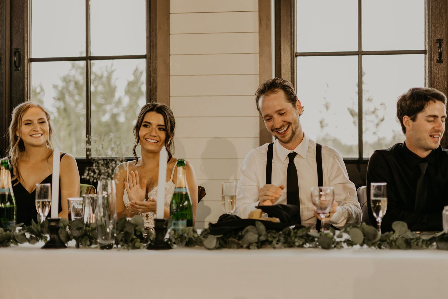 Wedding party seated at head table sharing laughs during reception celebration.