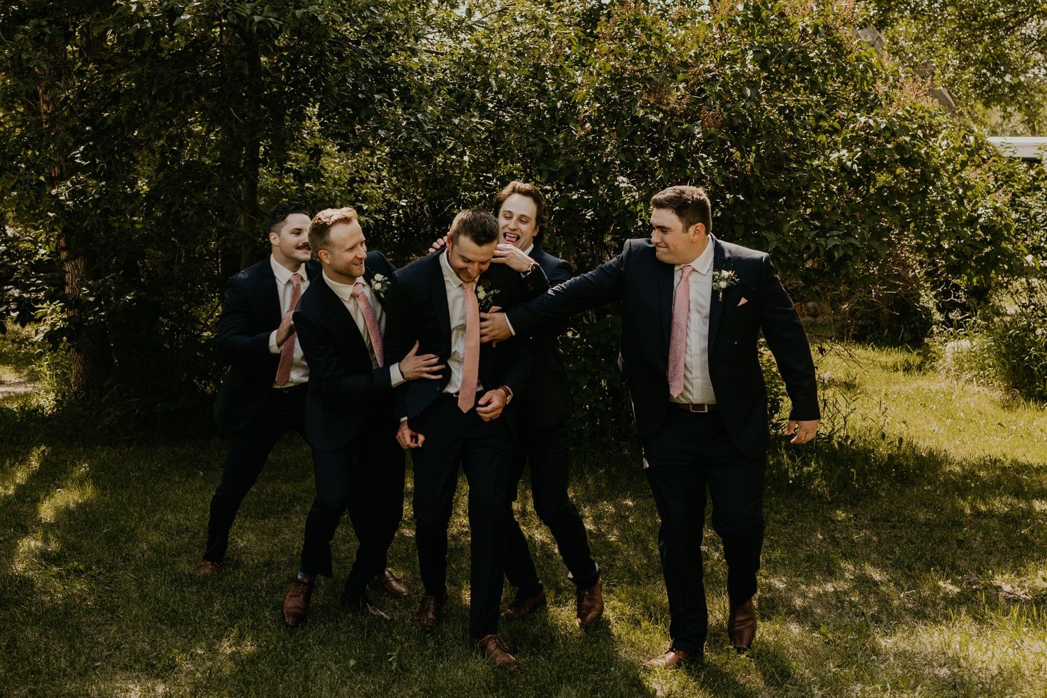 Groomsmen in dark suits having fun and laughing together outdoors.