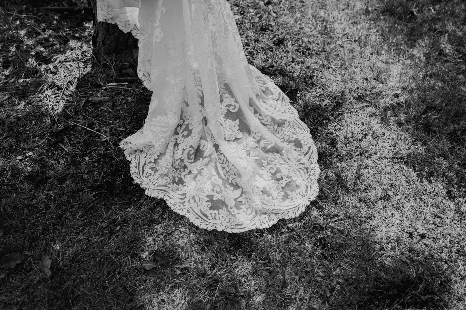 Close-up black and white detail of intricate lace wedding dress train on textured ground.
