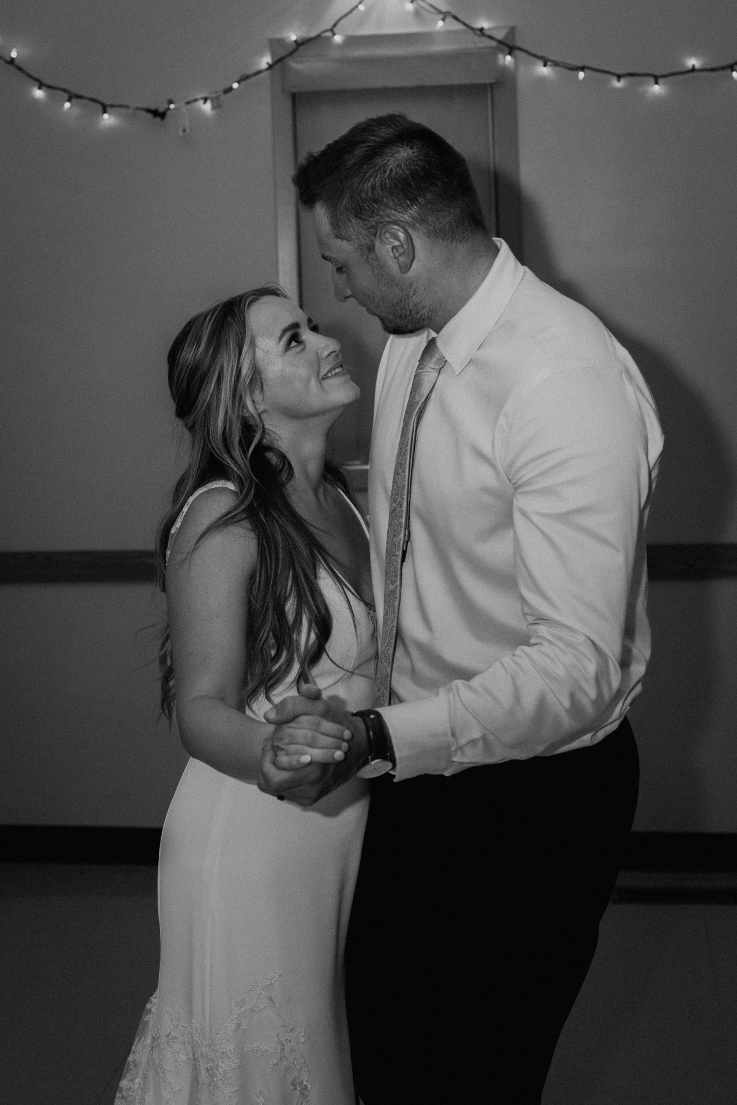 Romantic black and white dance photo under string lights at wedding reception.