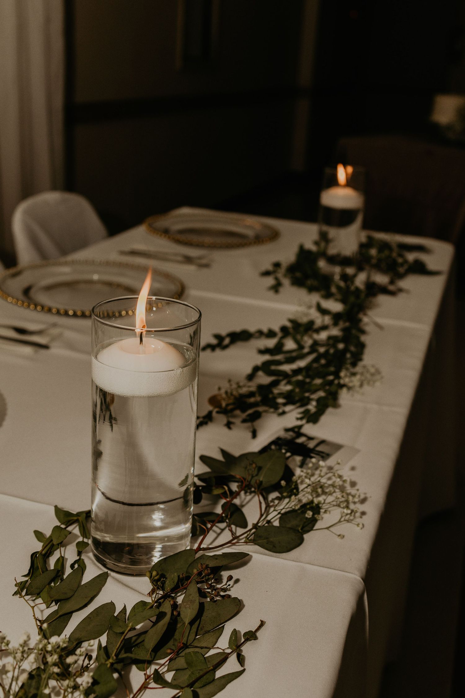 Elegant reception table with white candles and eucalyptus garland centerpiece.