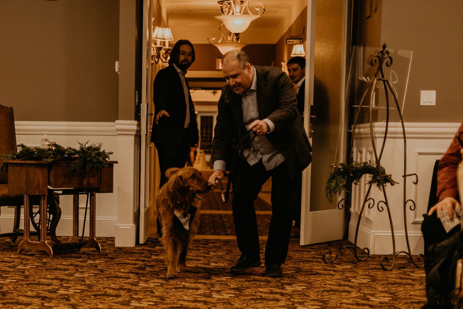 A golden retriever leads the way through an elegant hallway during a wedding celebration.