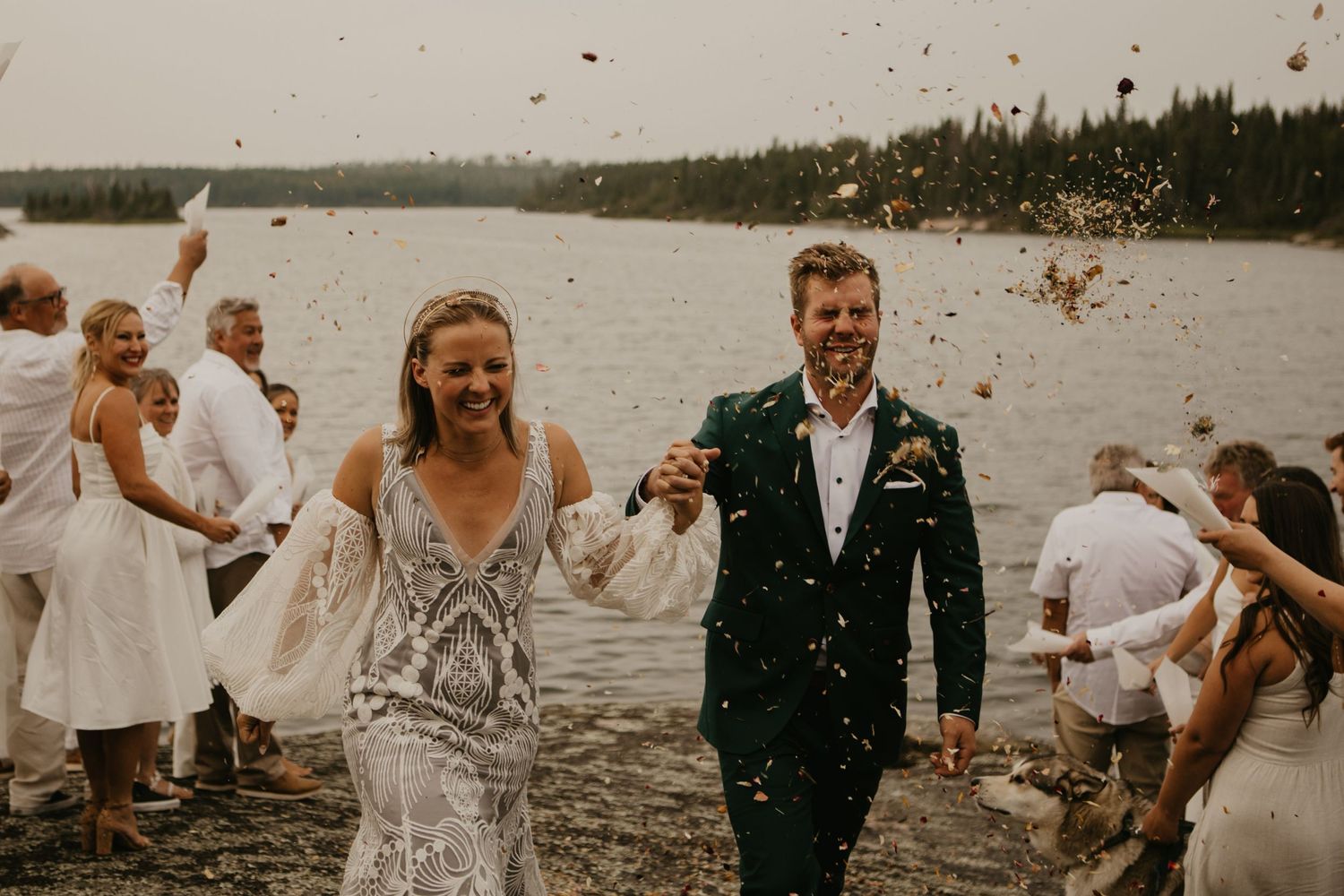 Newlyweds walking through confetti shower with wedding party celebrating by the lake.