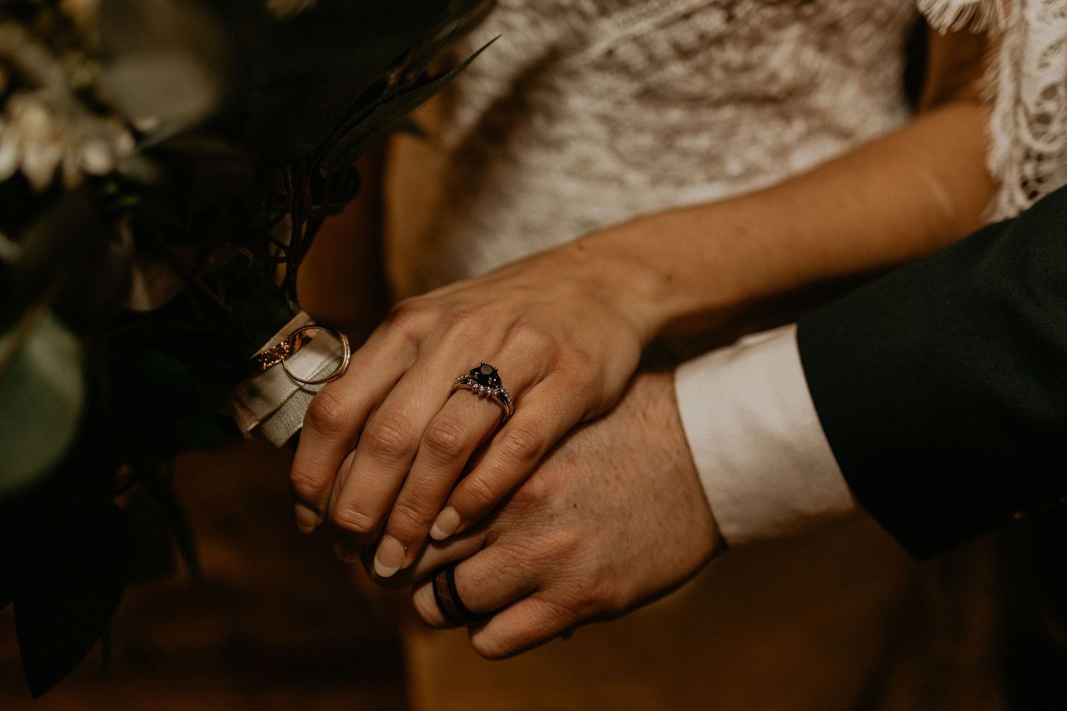 Close-up of newlyweds' hands with wedding rings and floral decor.