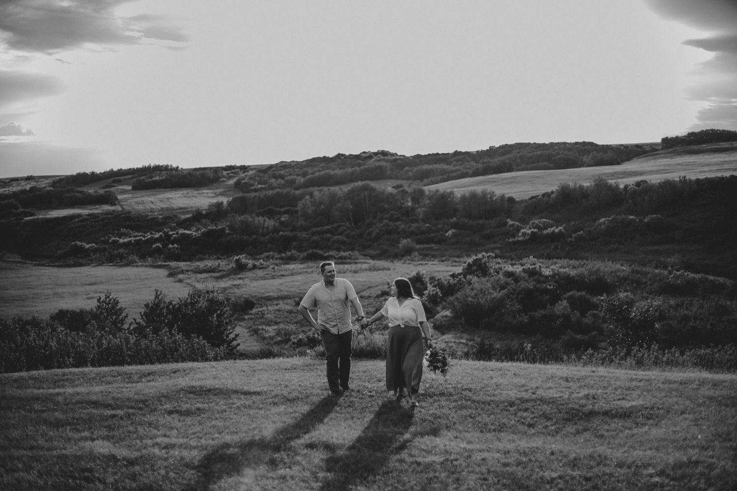 A couple strolls together along a scenic hilltop path in black and white.