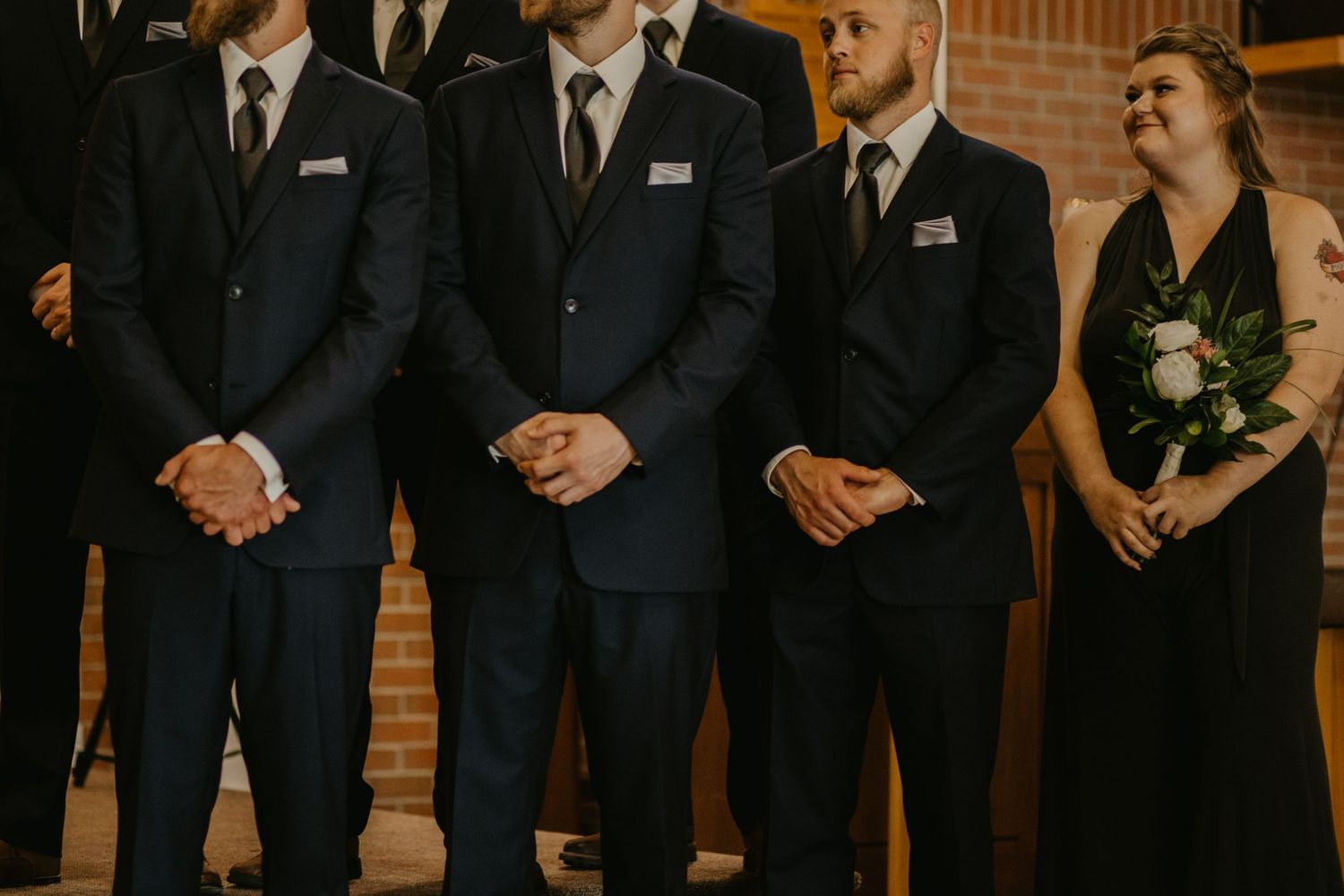 Wedding party members in navy suits stand in formation during the ceremony.