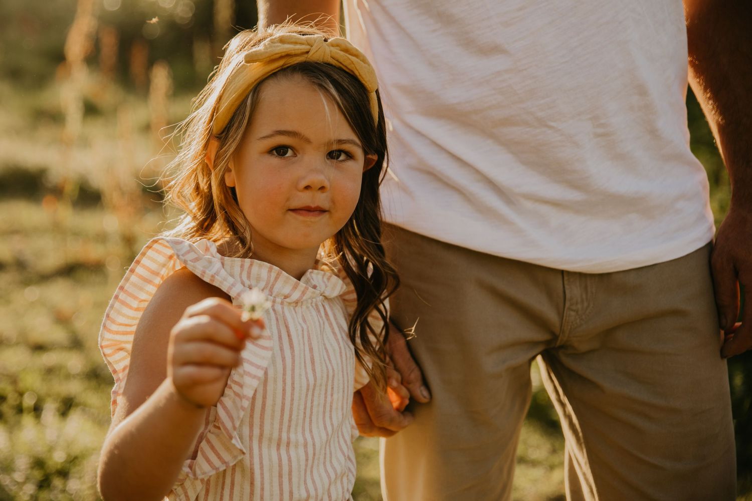 Child in striped dress enjoying golden hour sunlight outdoors.