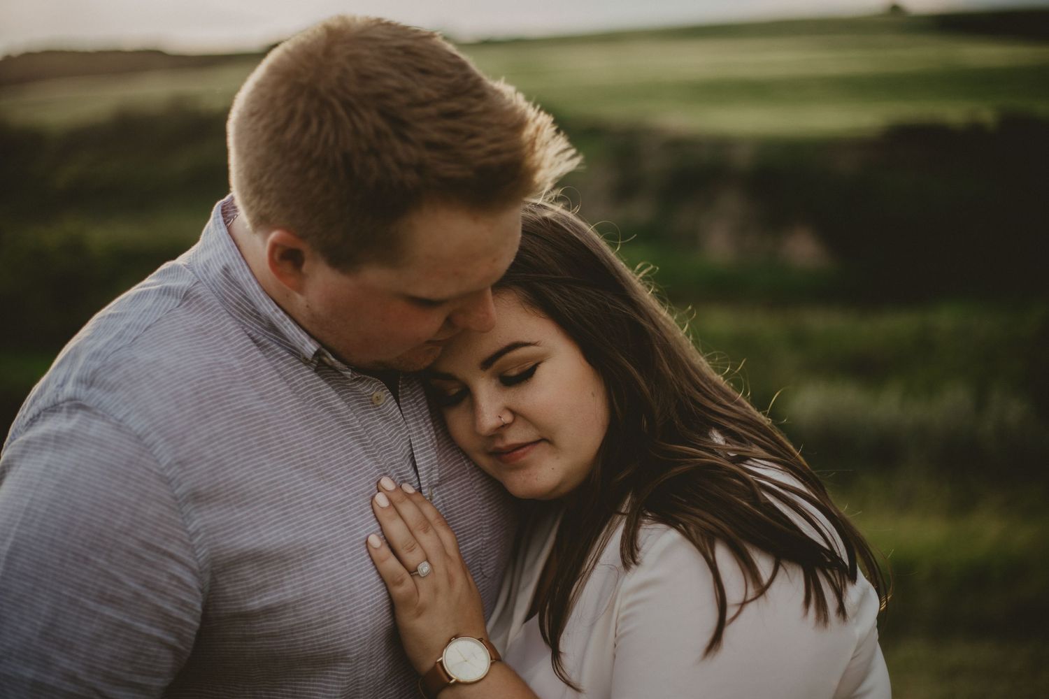 A romantic outdoor portrait of a couple embracing in a grassy field at golden hour.