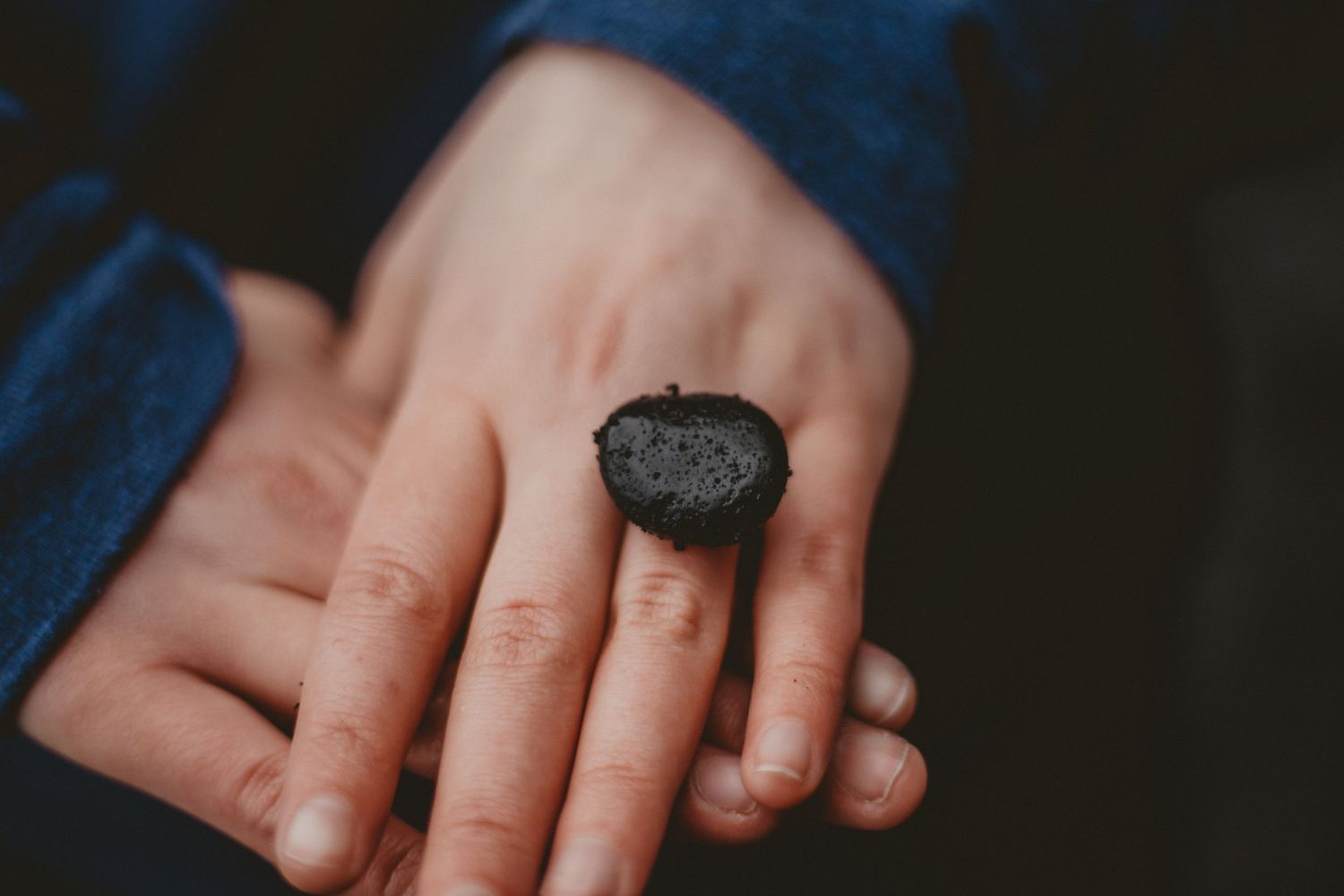 Close-up shot of a hand wearing a dark engagement ring against a blue sleeve.