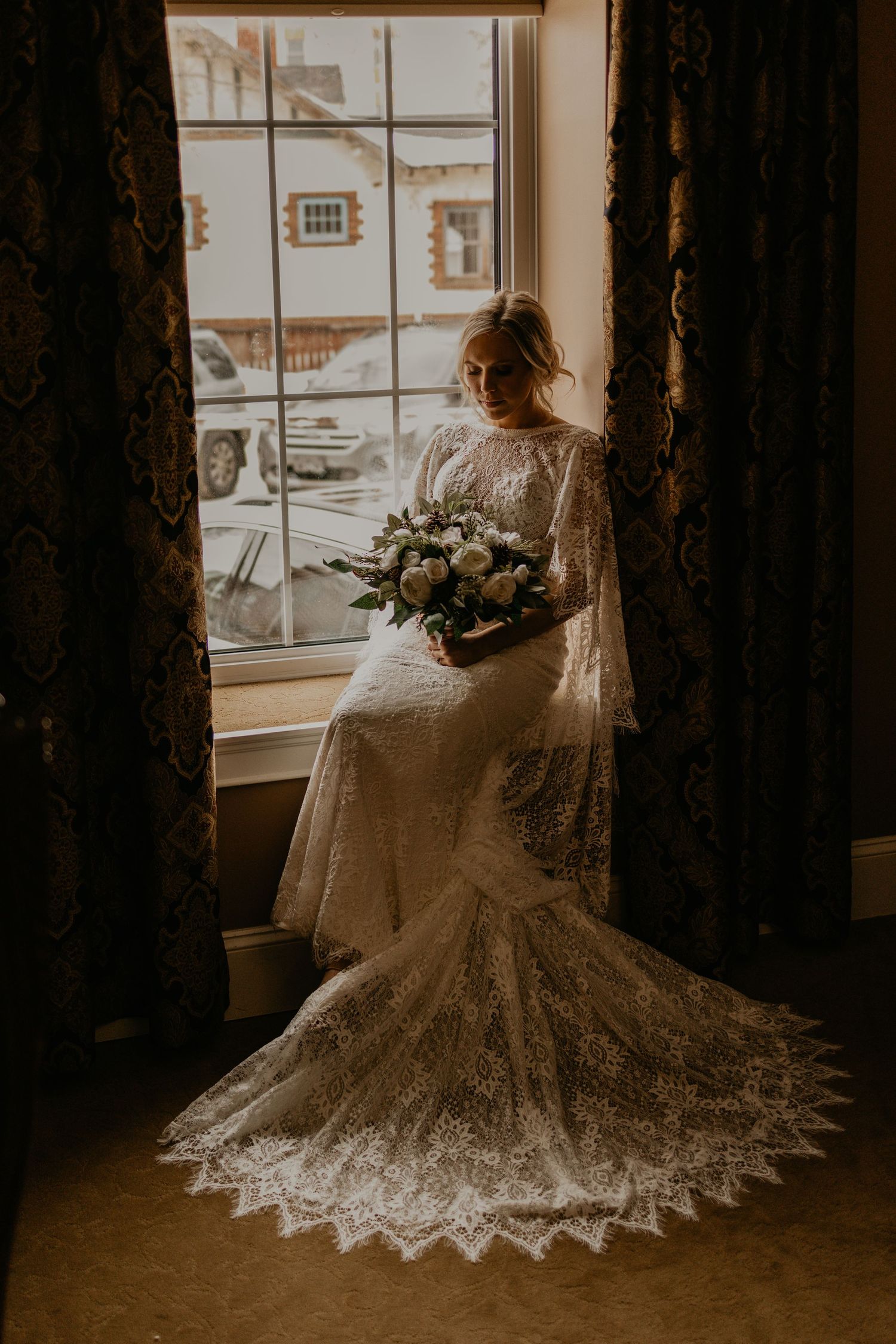 A wedding dress with intricate lace details and long train silhouetted against a bright window.