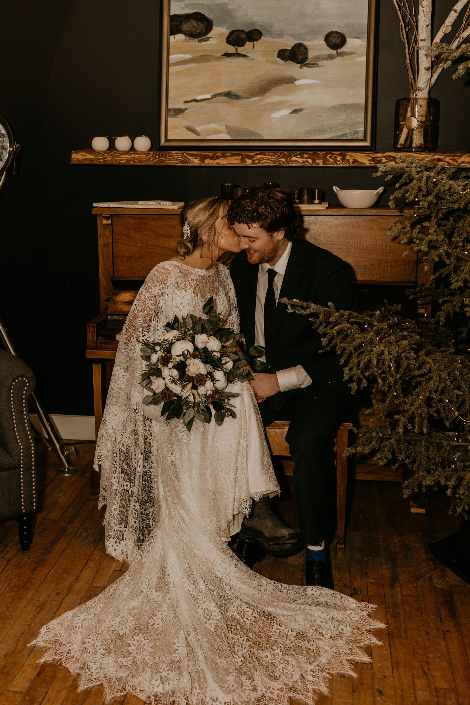 A romantic moment captured between newlyweds sitting at a vintage piano with a beautiful bouquet.