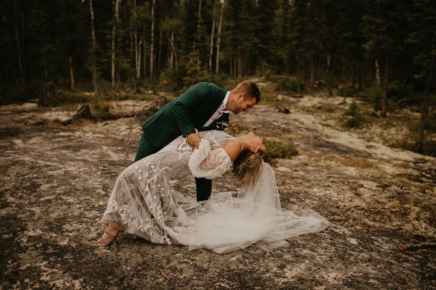 Artistic wedding photography with dramatic dip pose against forest background.