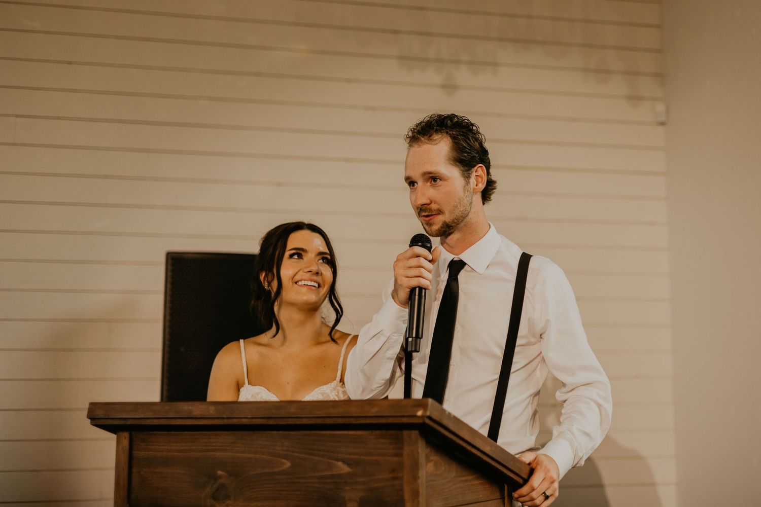 Couple delivers heartfelt speech at wooden podium during wedding reception.