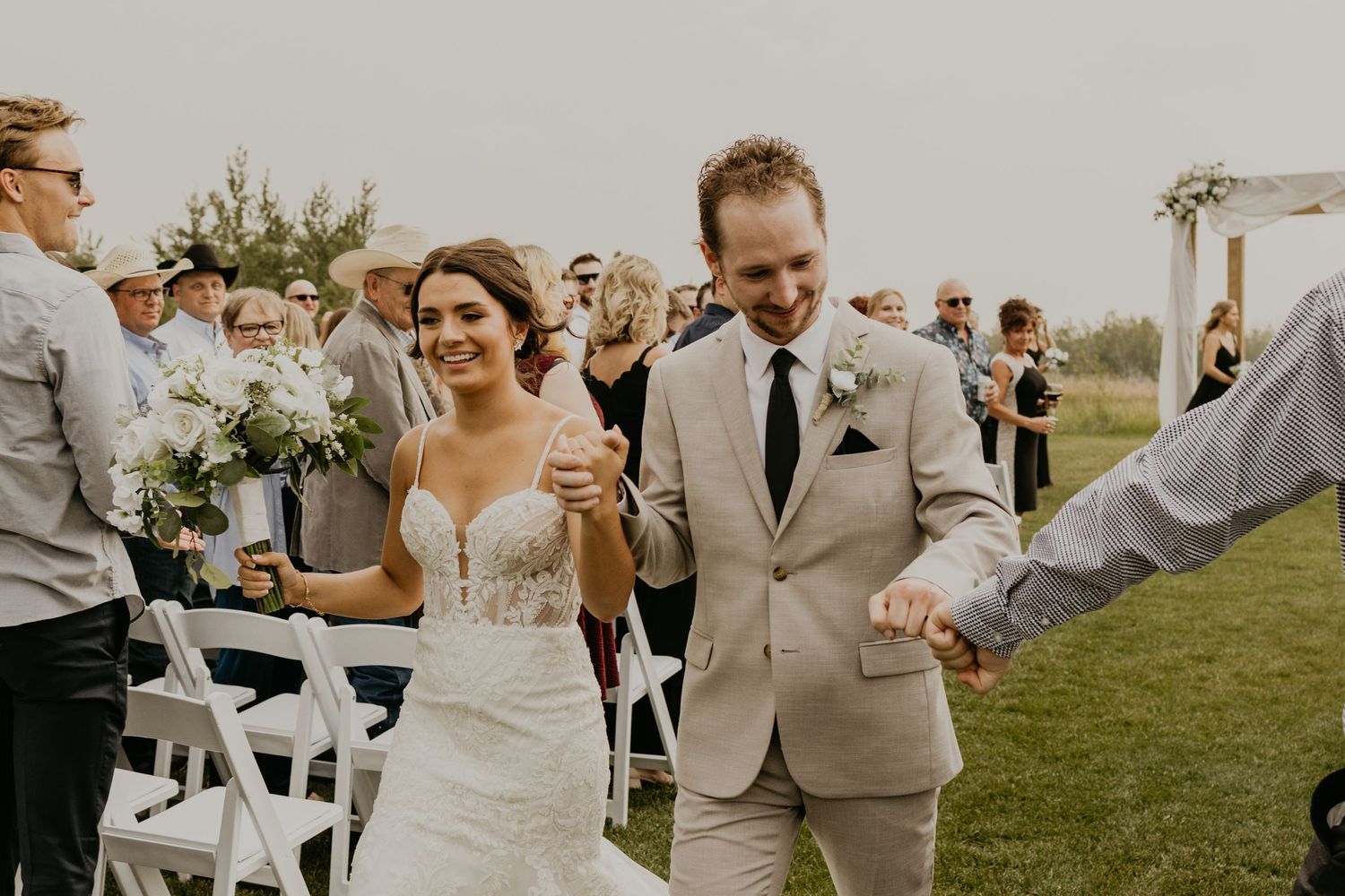 Wedding couple celebrates while walking down aisle after outdoor ceremony.