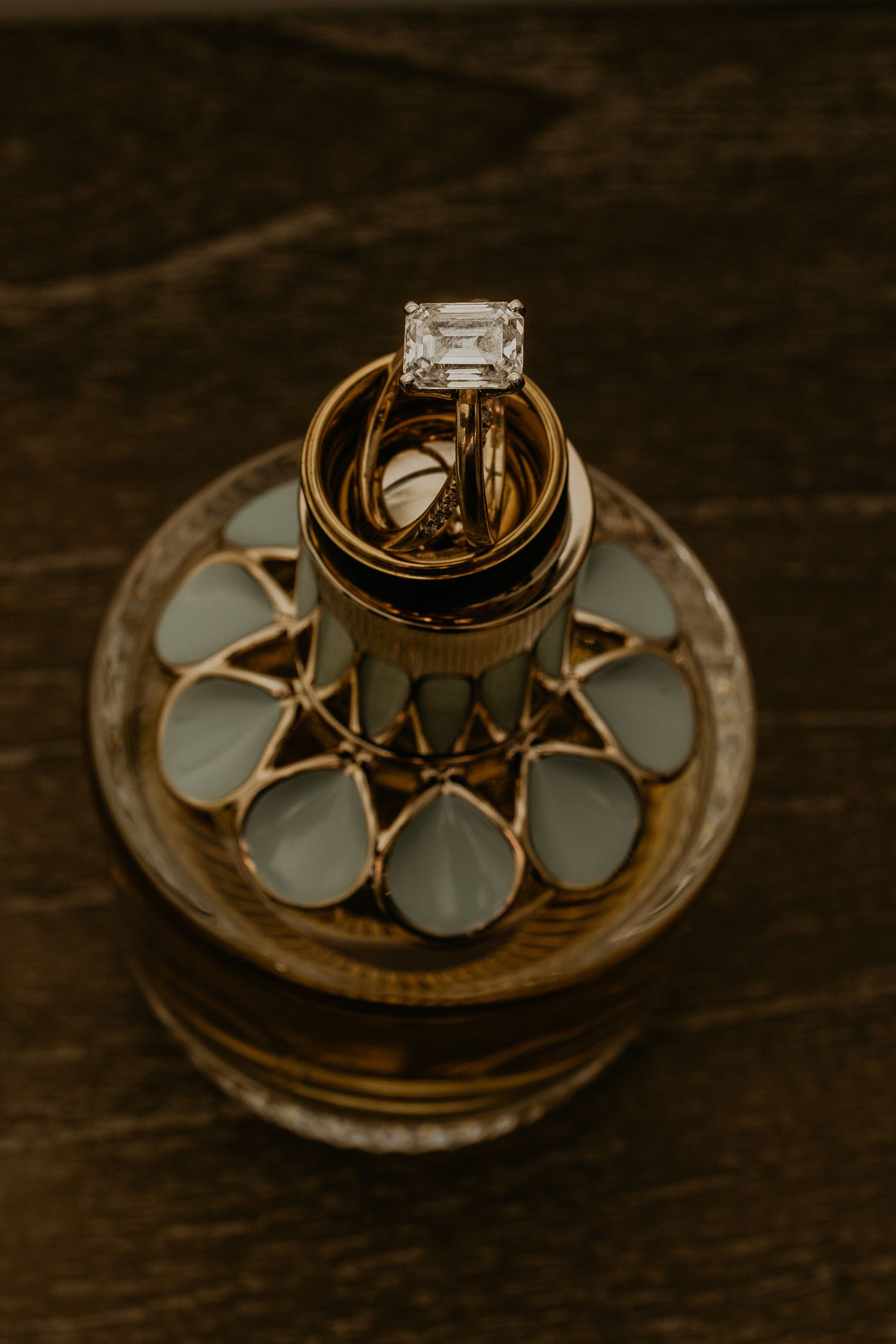 Wedding rings with diamond engagement ring displayed on decorative glass holder.