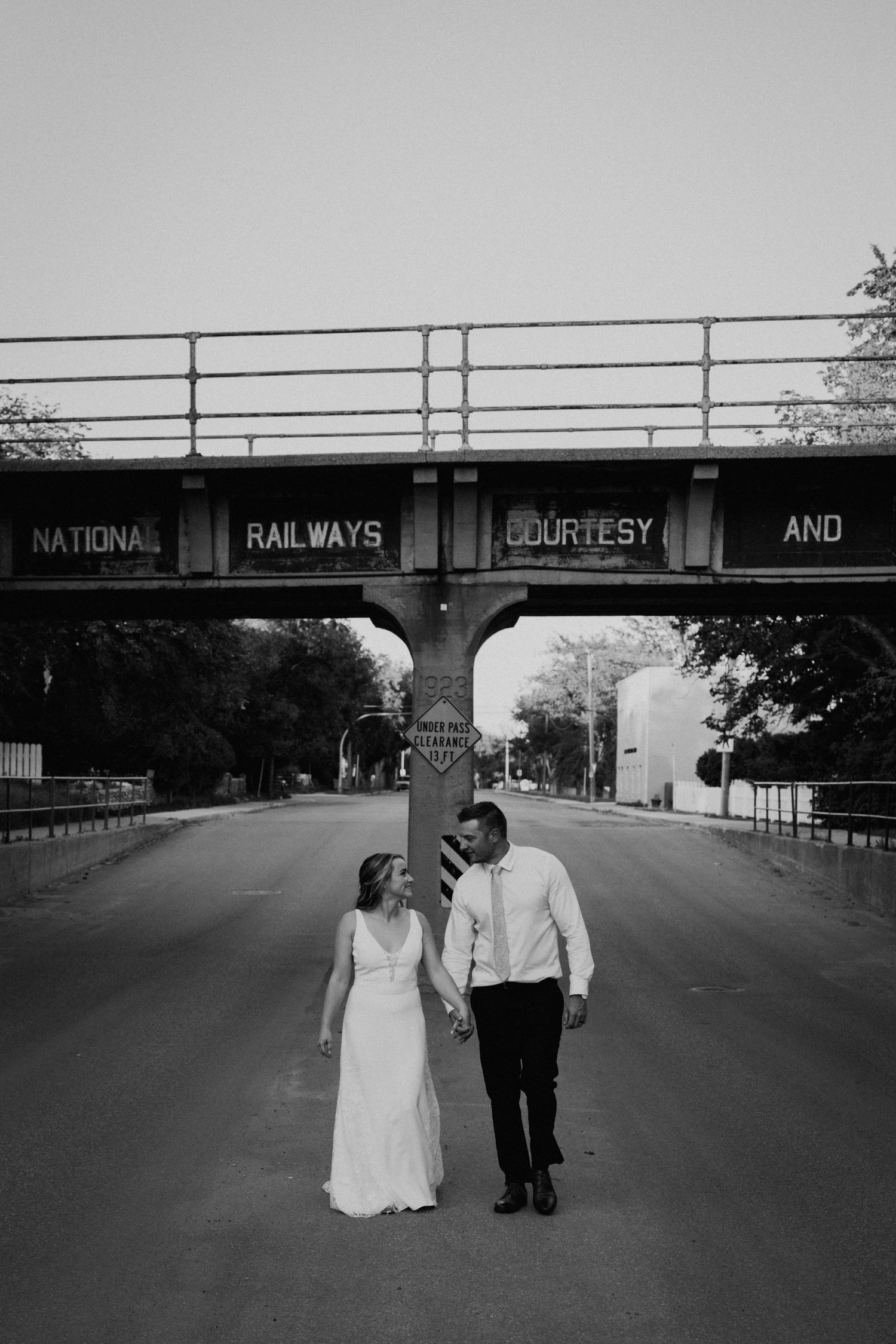 Black and white photo of couple walking under a National Railways bridge.