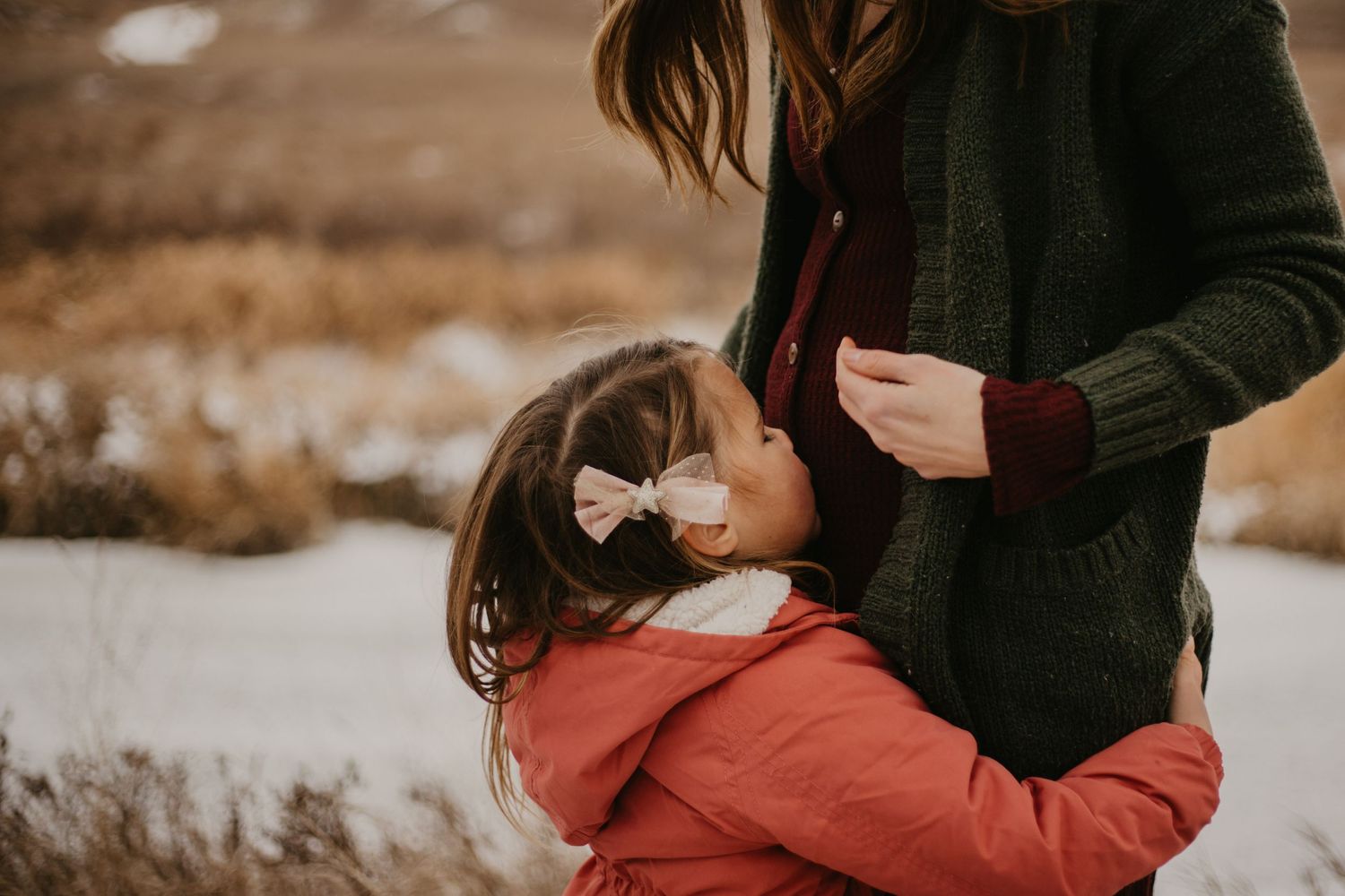 A tender moment between parent and child wearing winter coats against a muted winter landscape.