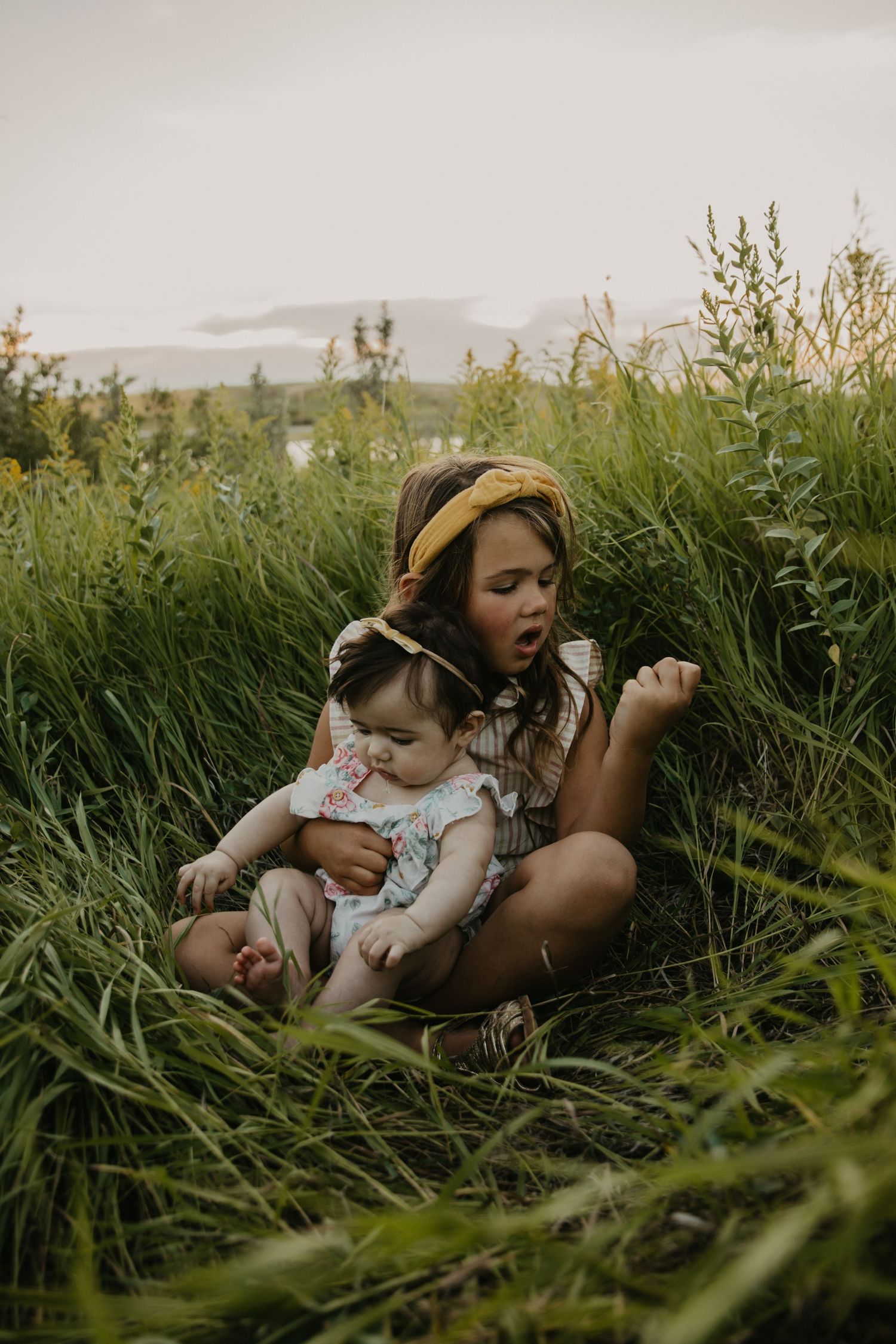 Two people sitting in tall grass during golden hour nature photoshoot.