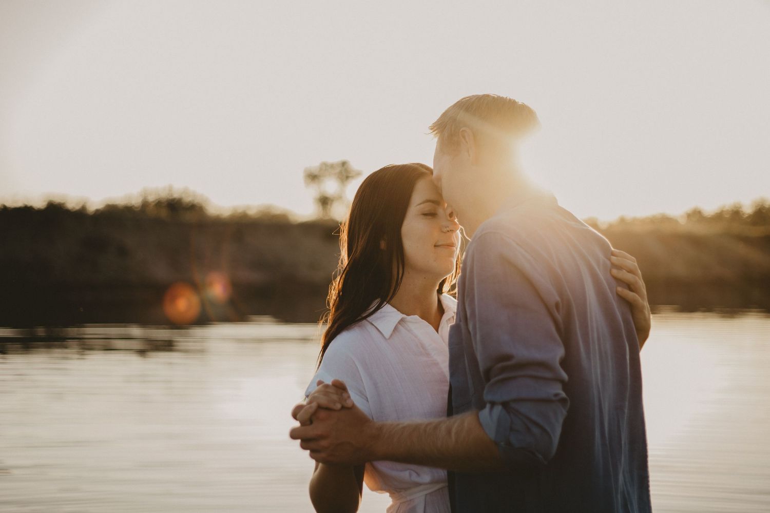 A silhouetted couple shares an intimate moment by the water during sunset.