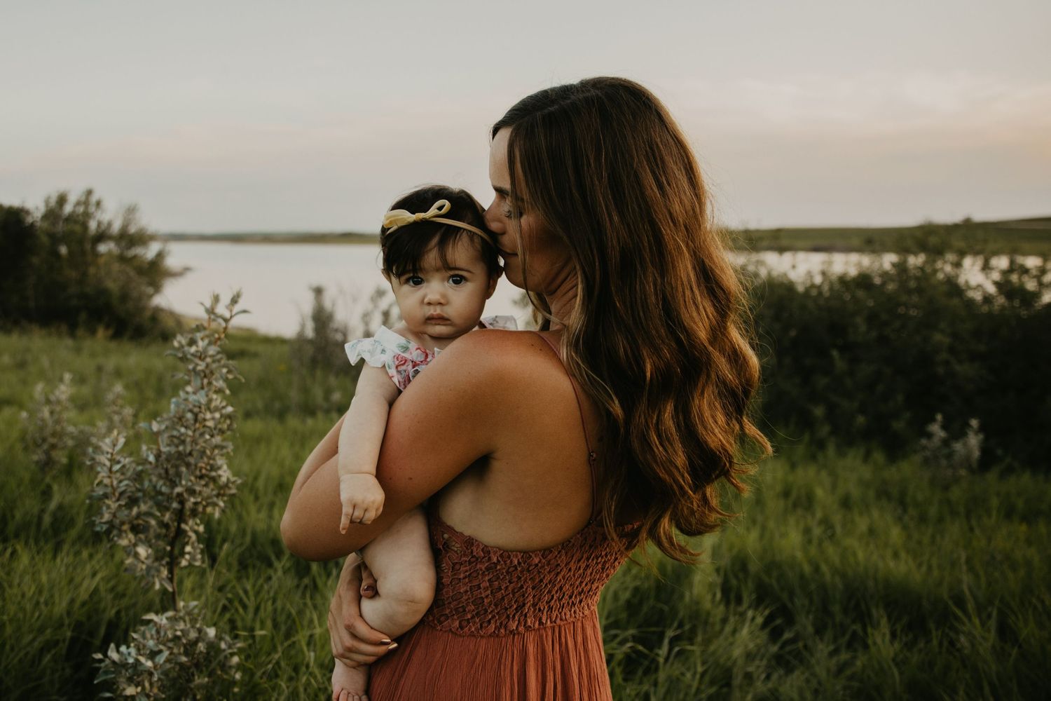 A tender embrace captured at sunset with a lake and rolling hills in the background.