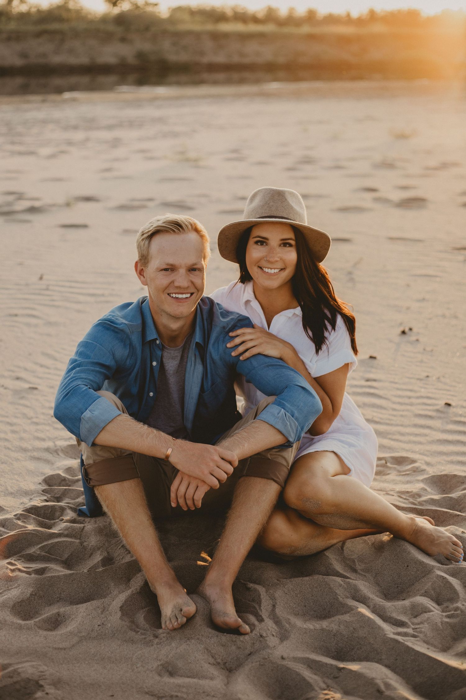 A joyful beach portrait of a couple sitting on the sand during sunset.