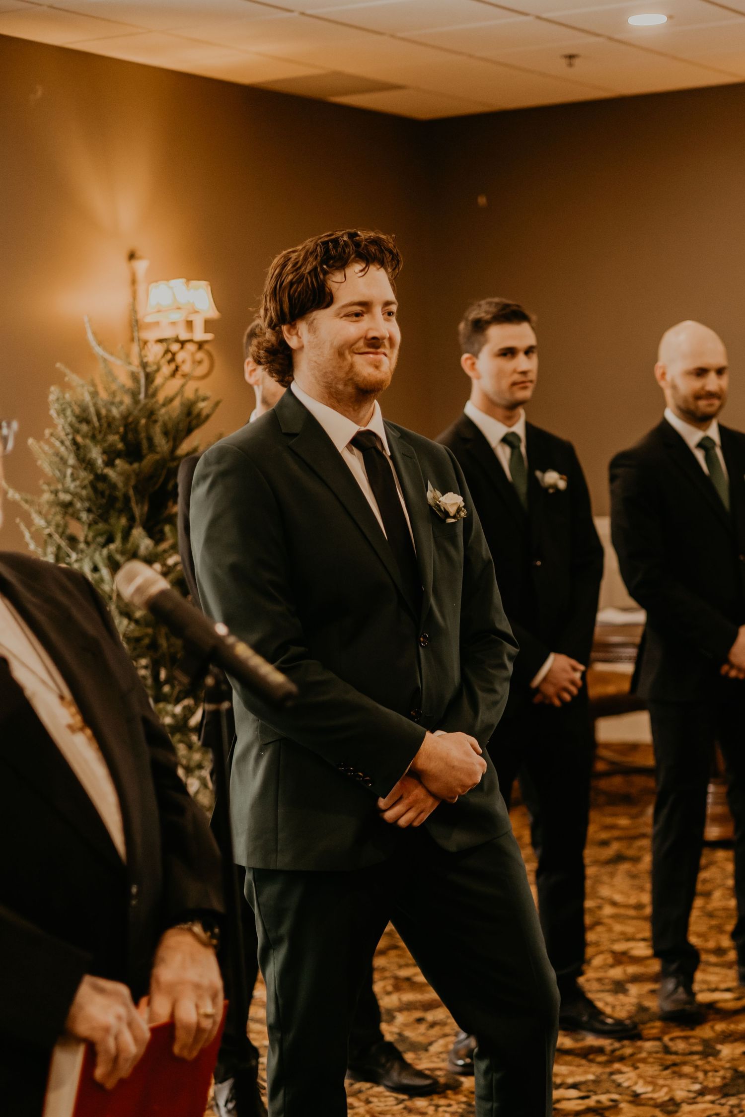 Wedding party members in dark suits stand at the front of an elegant ceremony space.