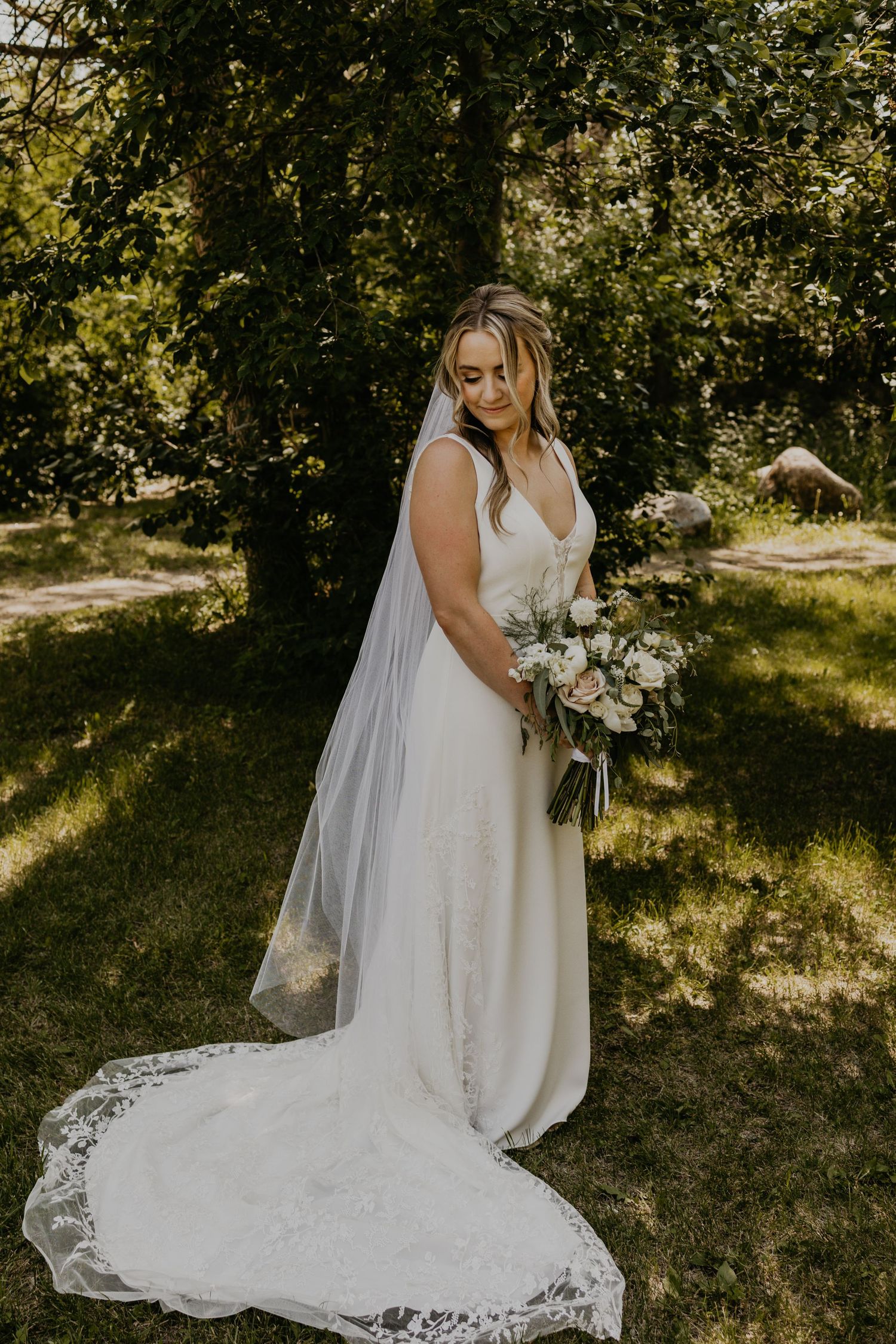 Bride in classic white gown with long train poses in dappled sunlight.