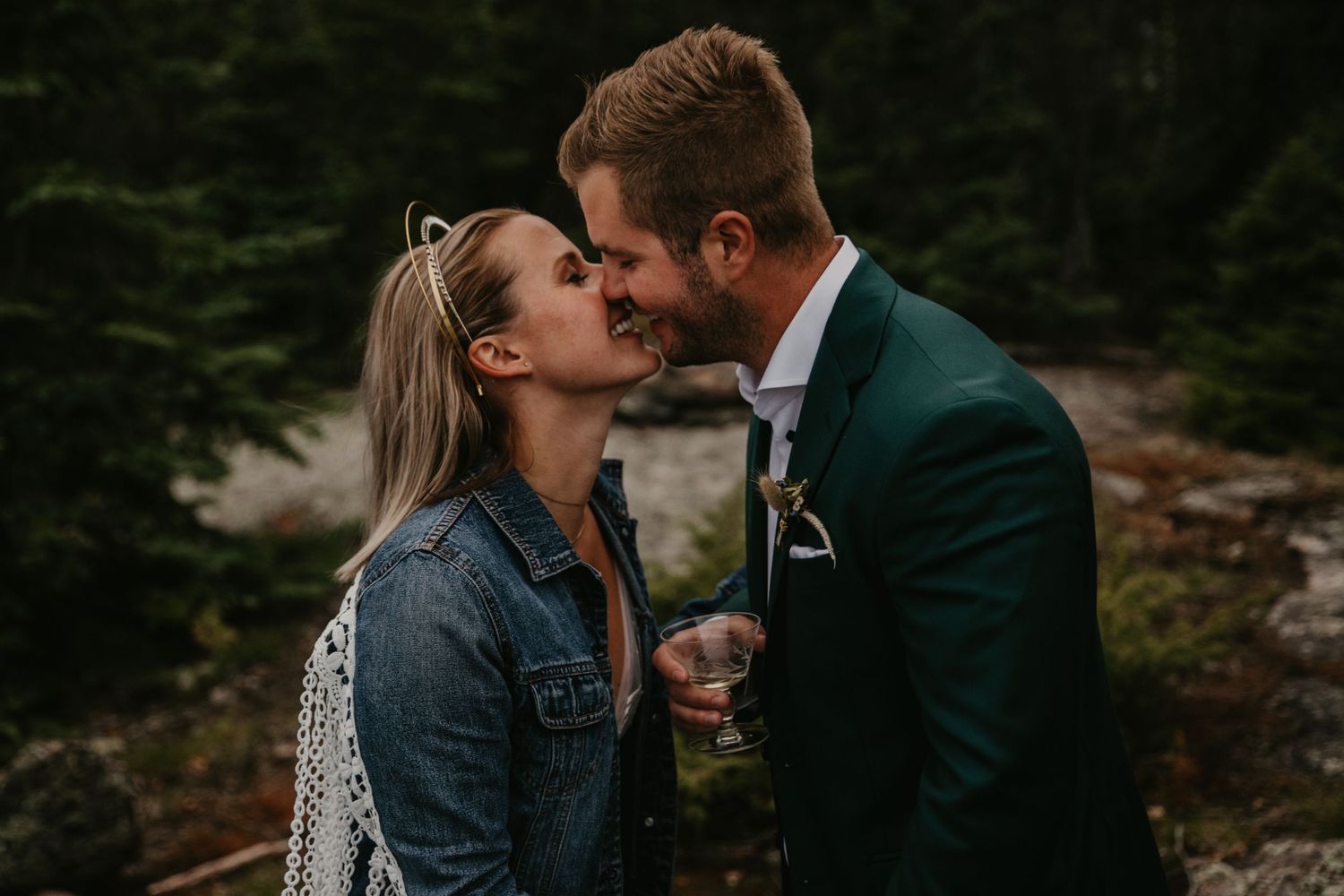 A romantic moment between a couple in formal wear and denim against an evergreen forest backdrop.