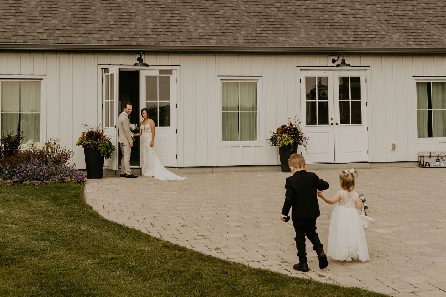 White farmhouse wedding venue with guests on curved stone pathway.