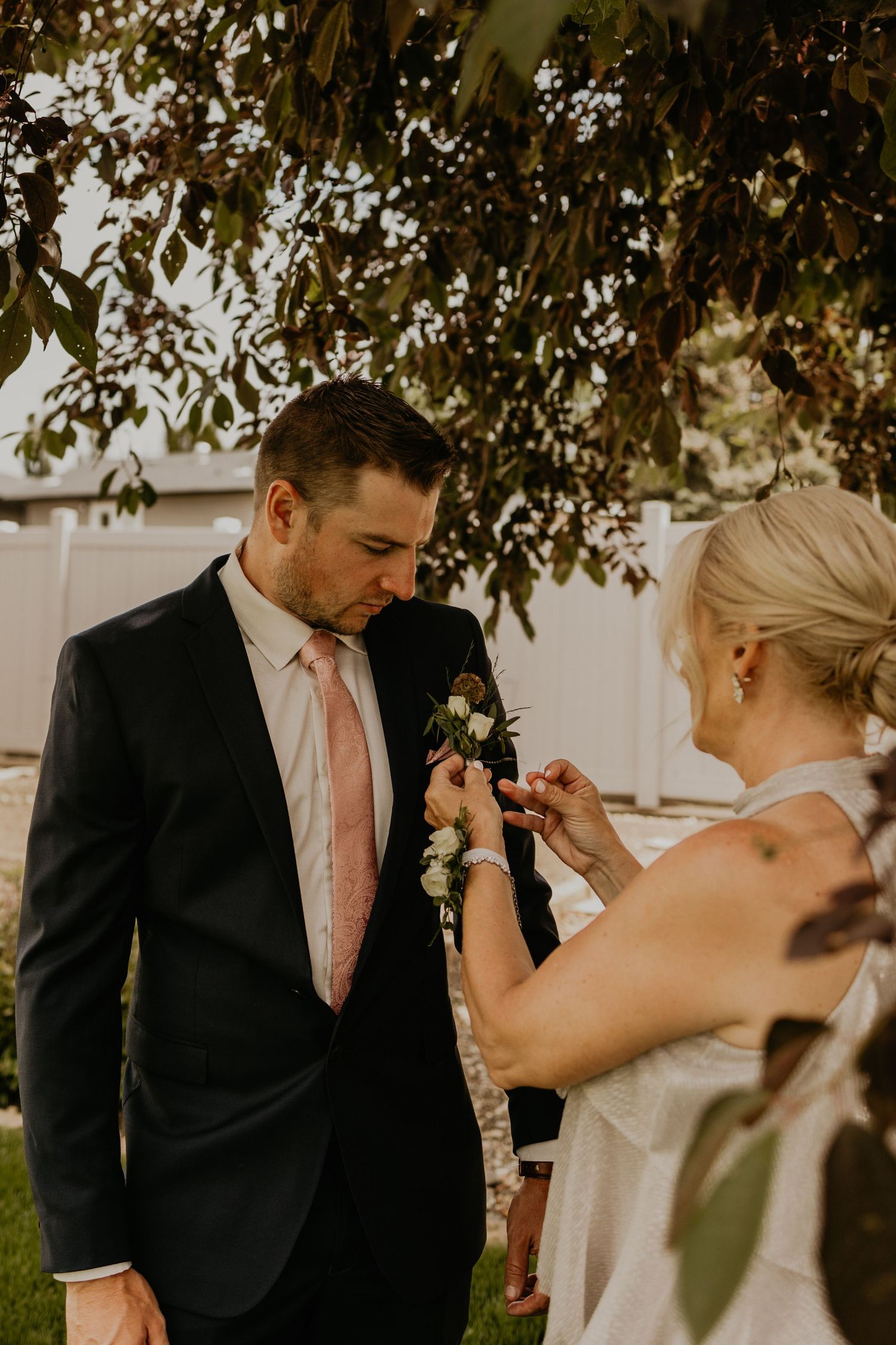 Wedding preparation moment showing boutonniere being pinned on groom's lapel in garden.