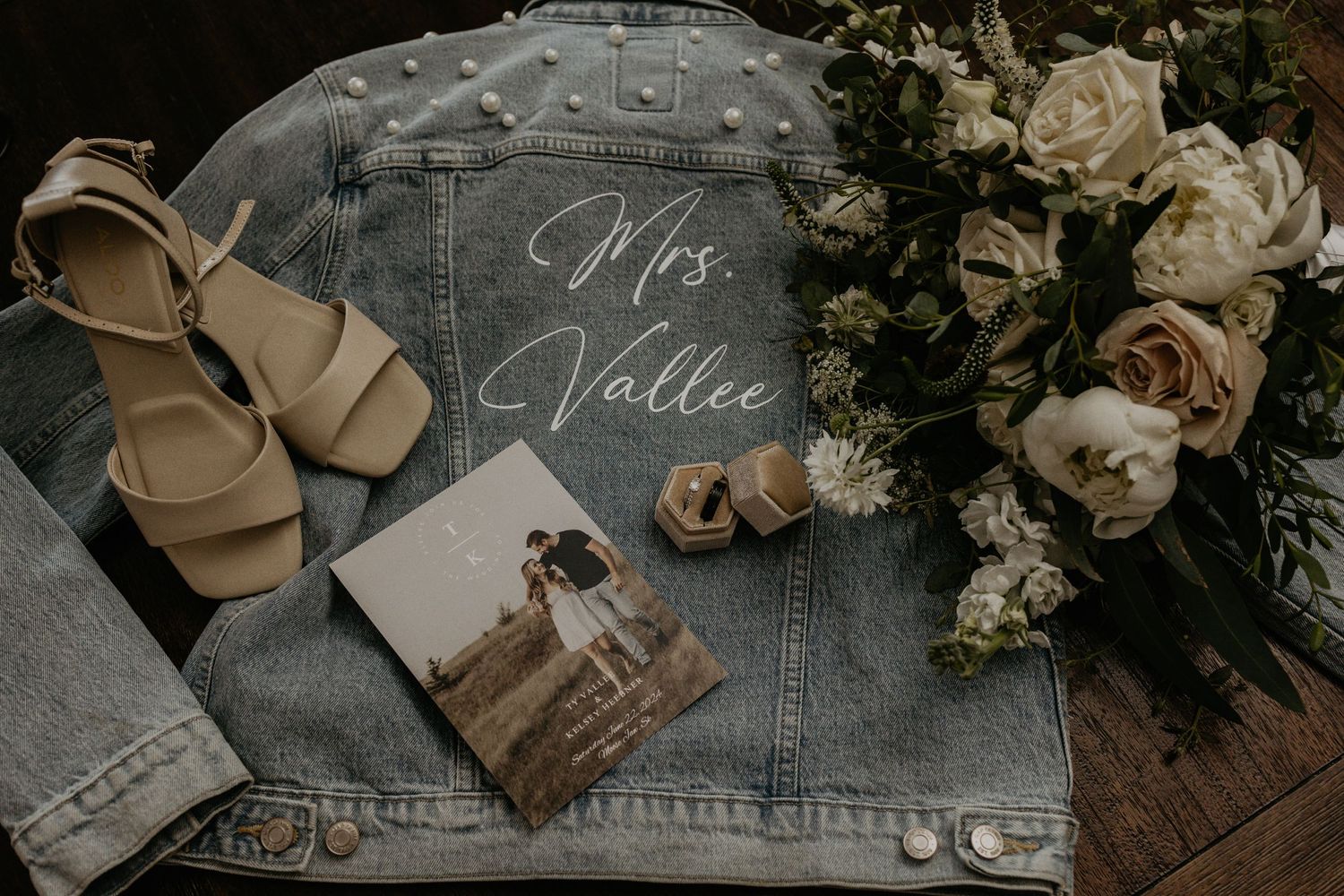 Wedding details flatlay with denim jacket, sandals, roses and a photograph.
