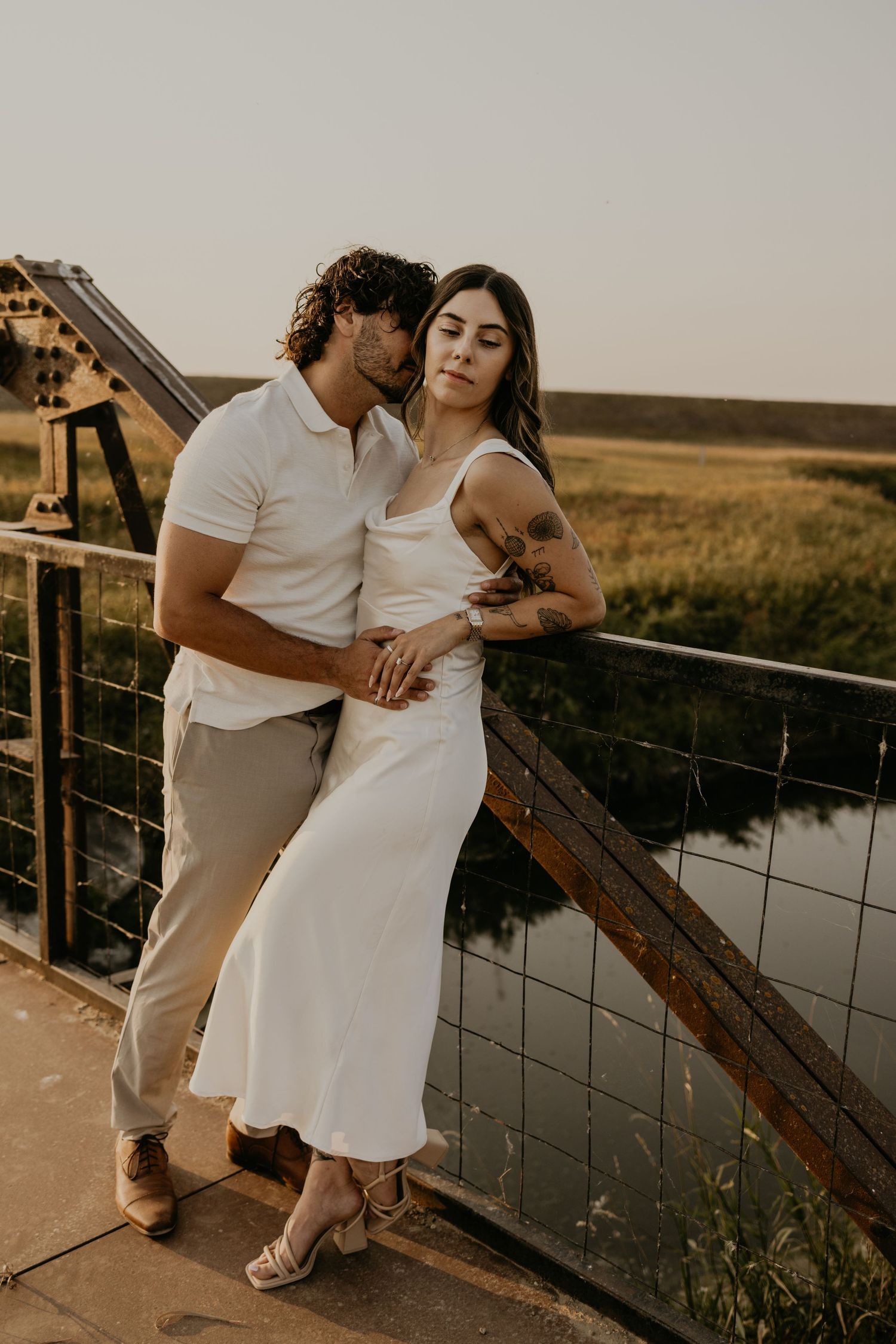 Couple in matching white outfits embracing on a wooden deck during golden hour.