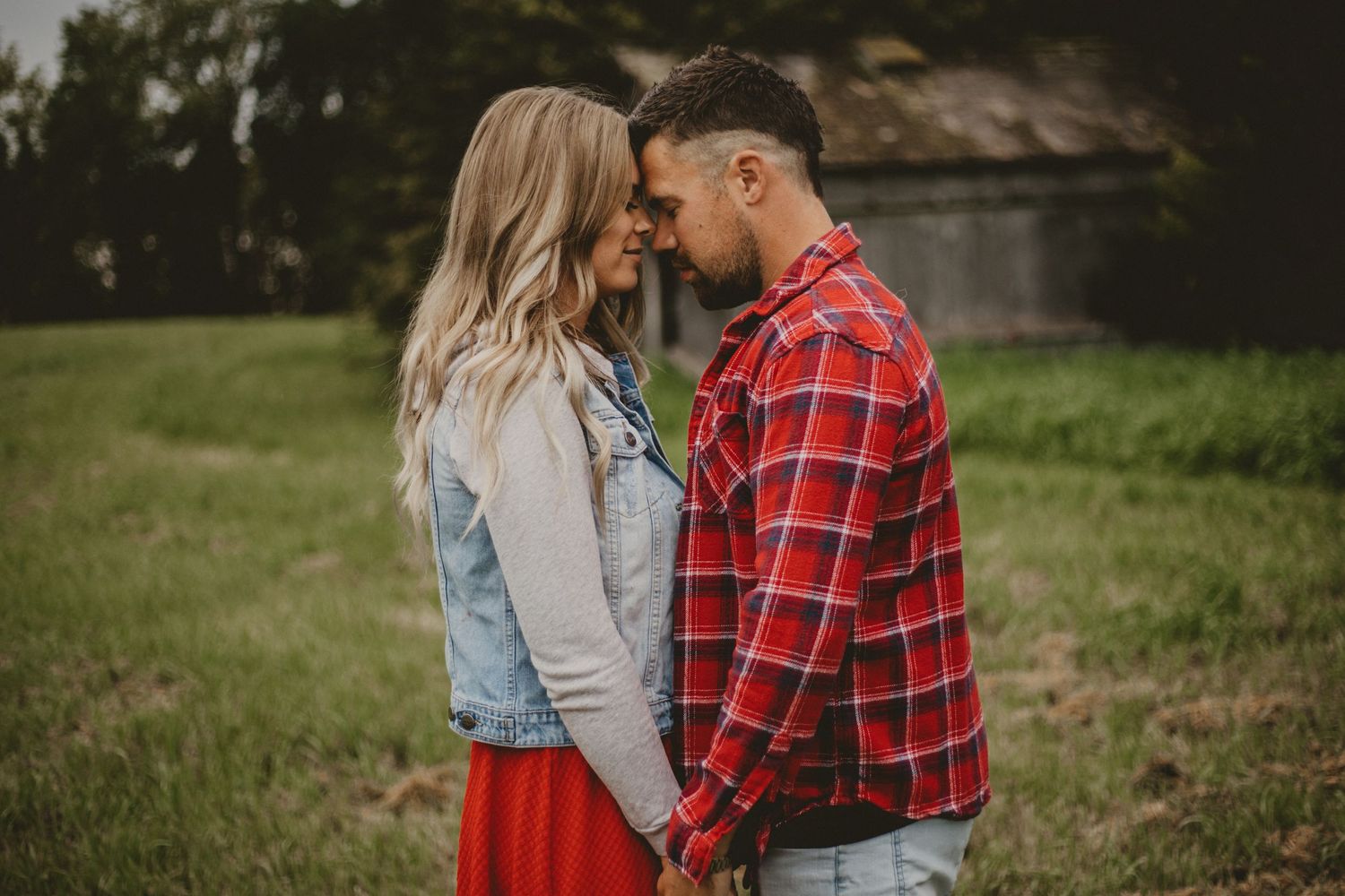 A tender moment between a couple wearing plaid and denim against a rural backdrop.