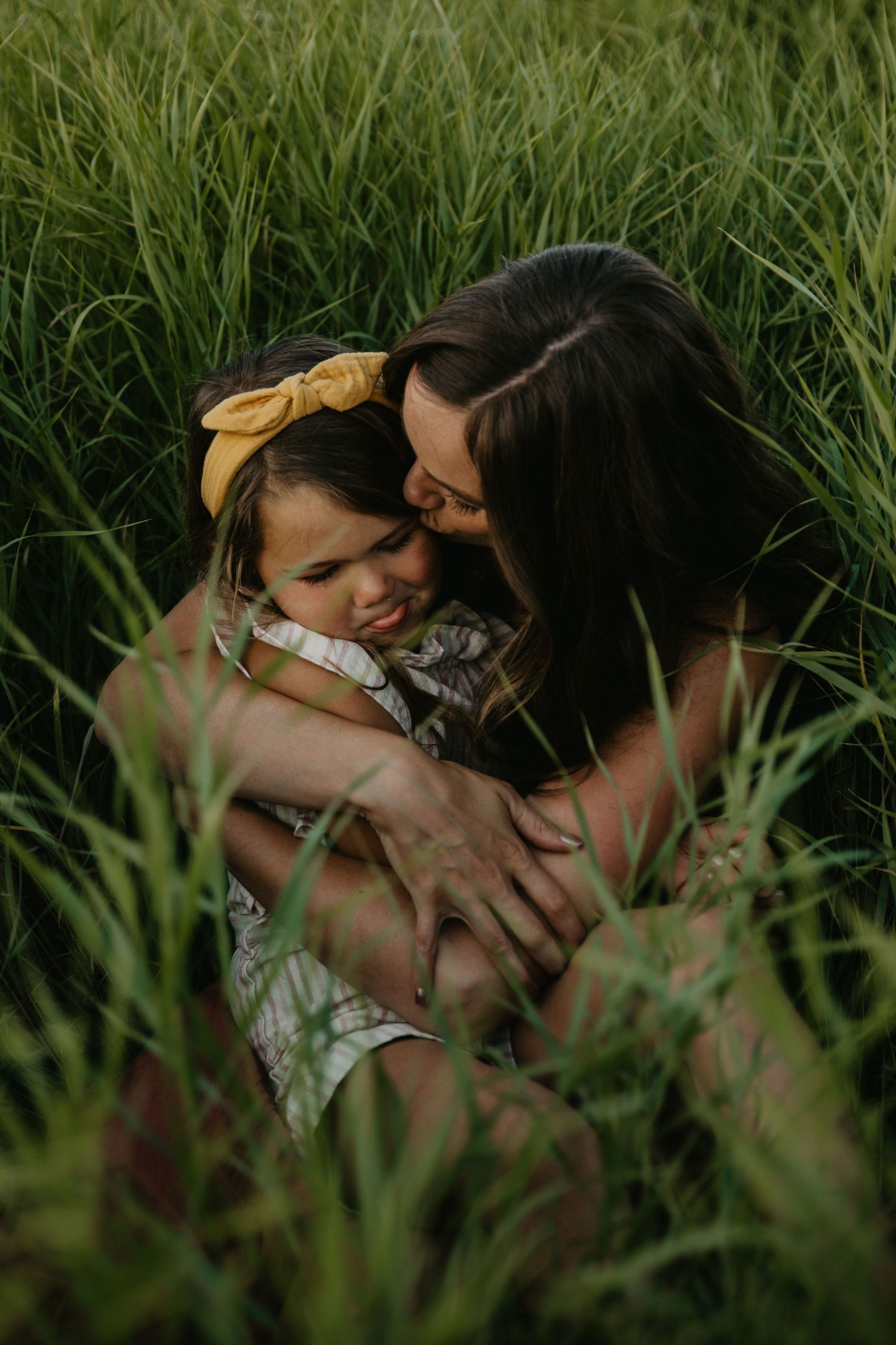Loving embrace captured in tall summer grass during golden hour photoshoot.