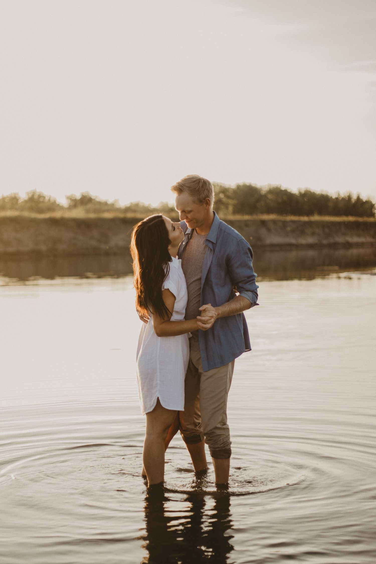 A romantic embrace in knee-deep water during golden hour at the beach.