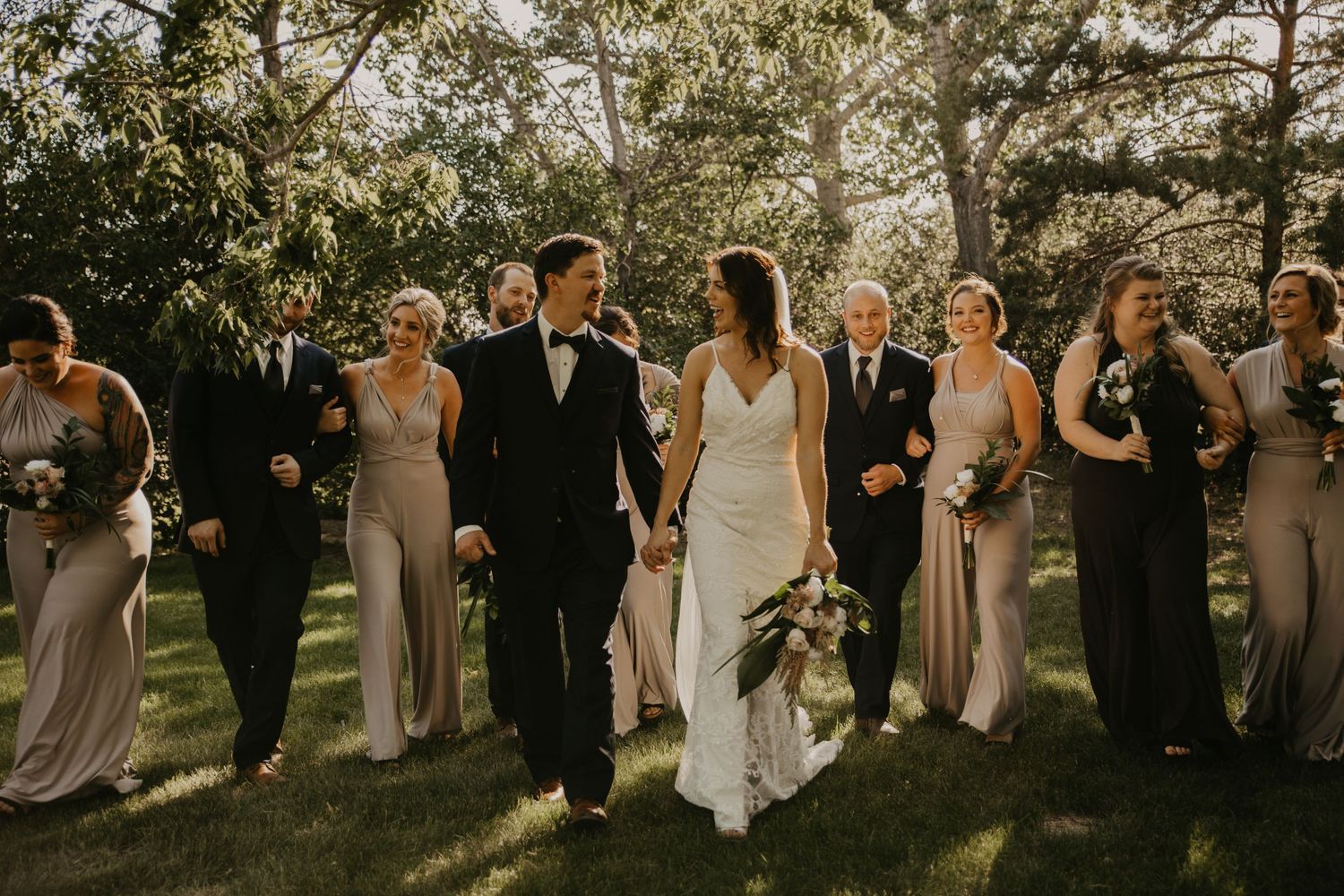 Wedding party walks together on grassy lawn in coordinated formal attire at outdoor ceremony.