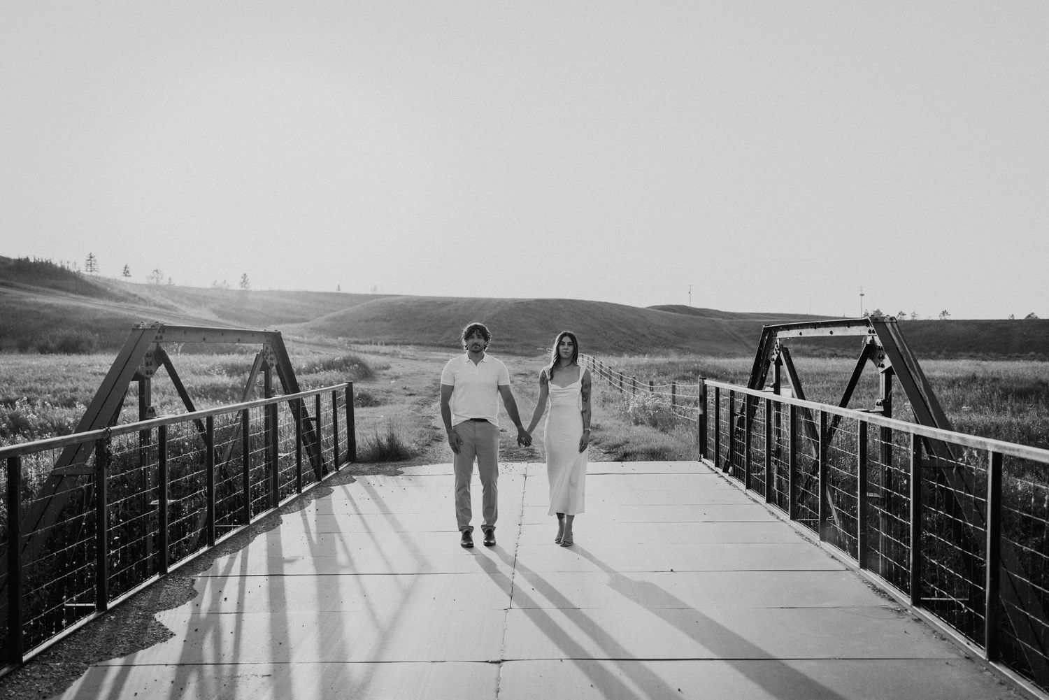 Silhouettes of people walking on a bridge pathway against a bright outdoor background.